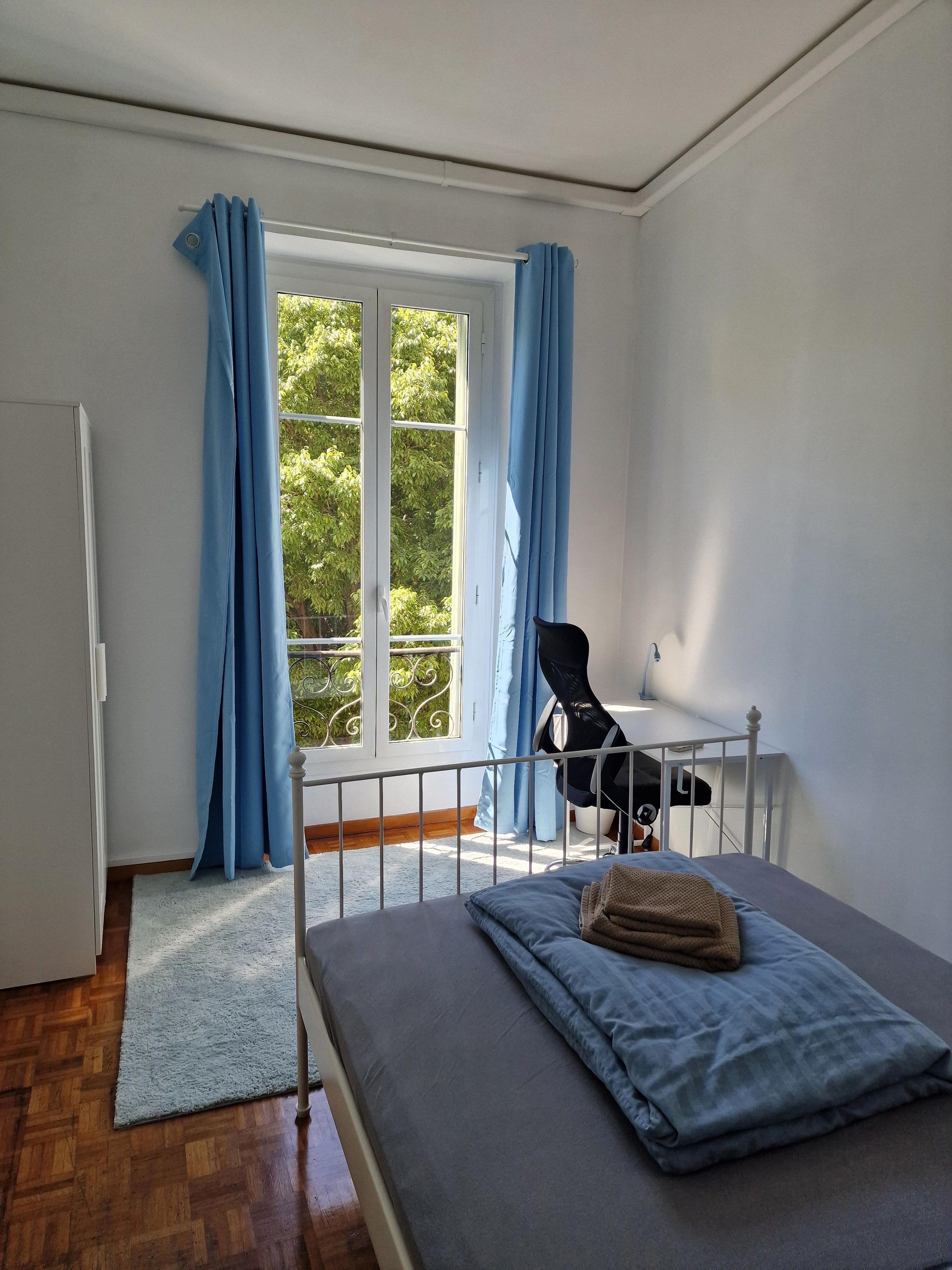 Private room Promenade showing bed, window with blue curtains and parquet floor