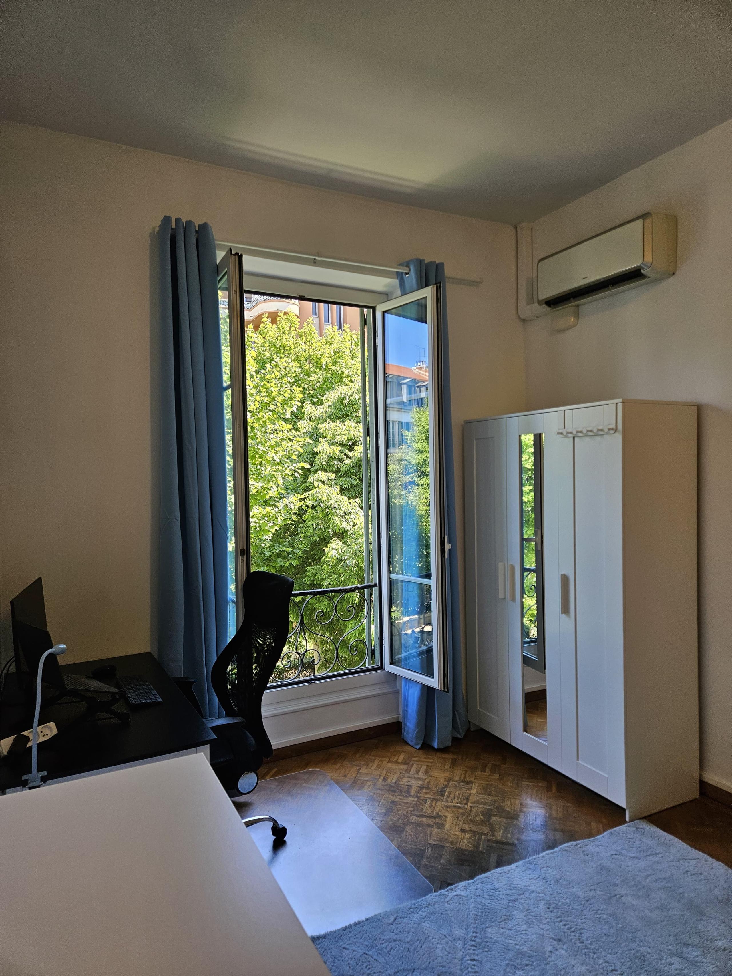Private room Mont Boron showing open window with blue curtains, white wardrobe with mirror, AC unit and ergonomic desk