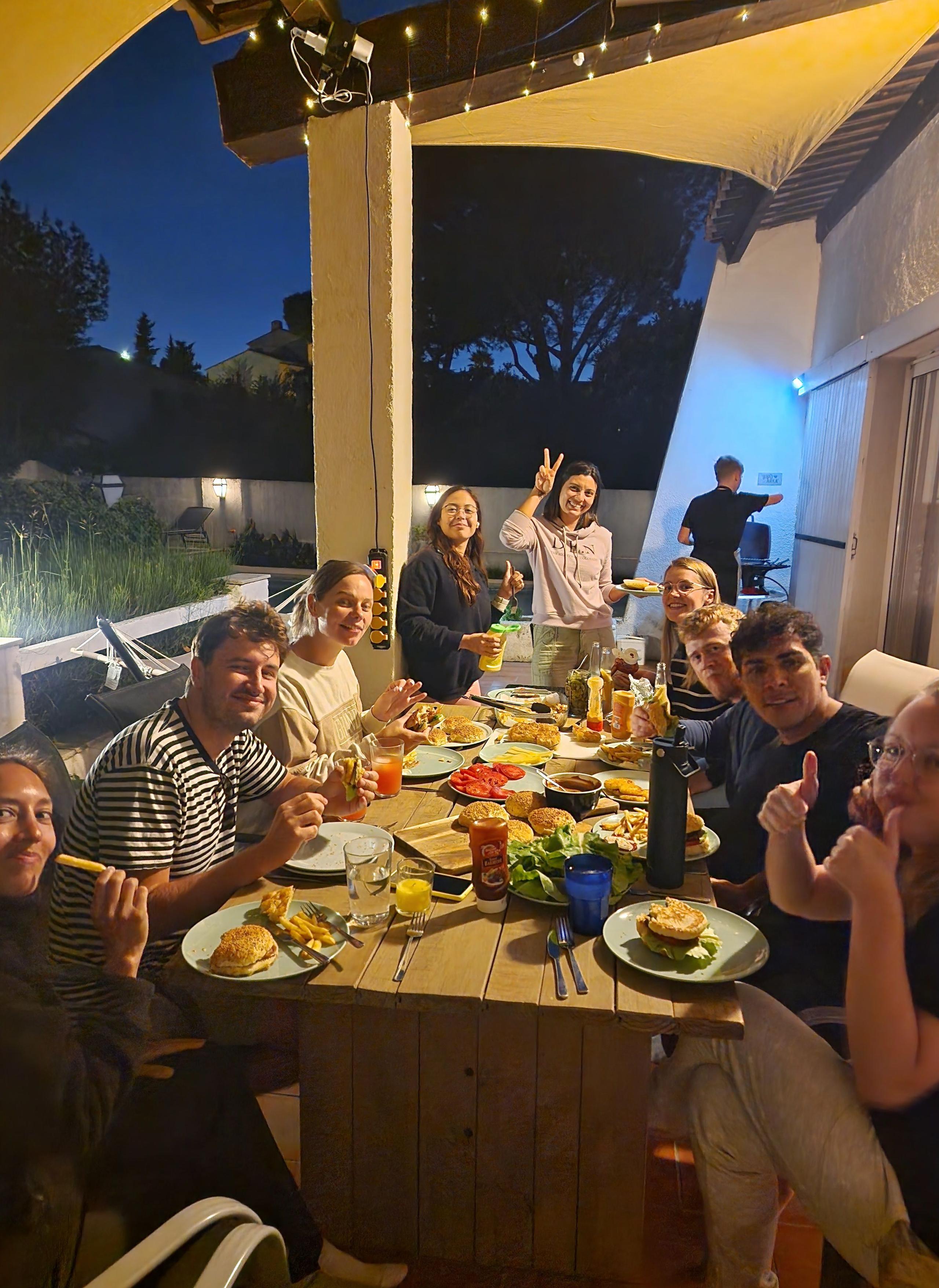 Group of coliving residents sharing a meal together at the outdoor terrace table at night