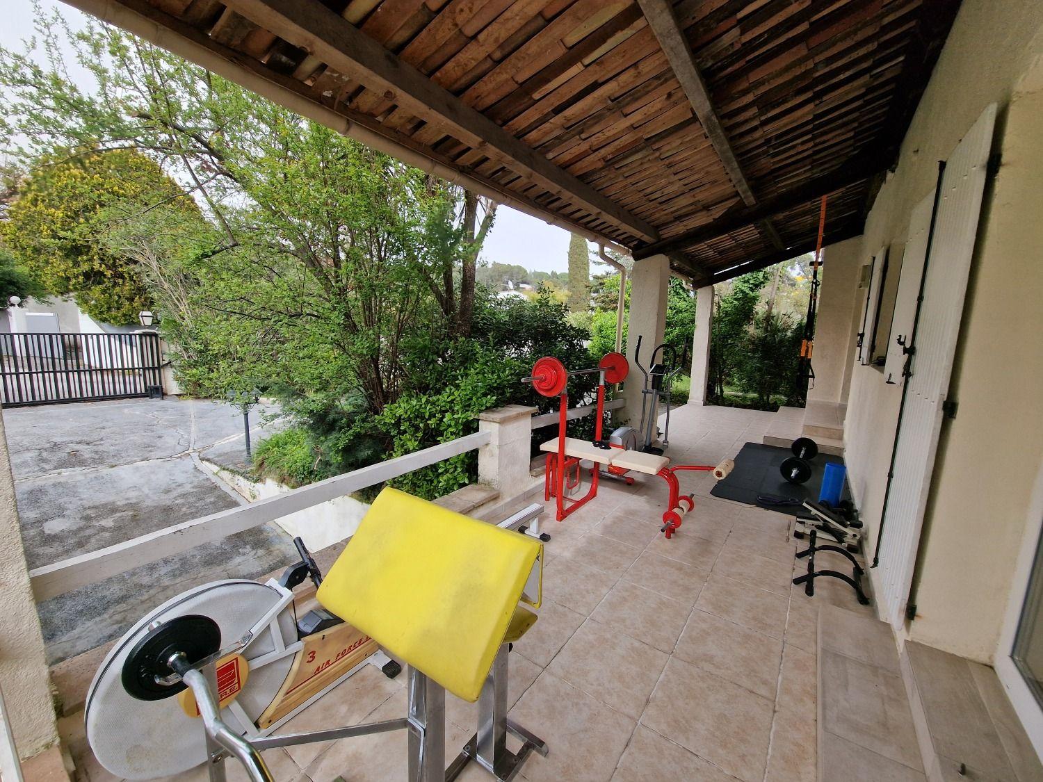Outdoor fitness corner with gym equipment including weights, benches, and elliptical machine under a covered area