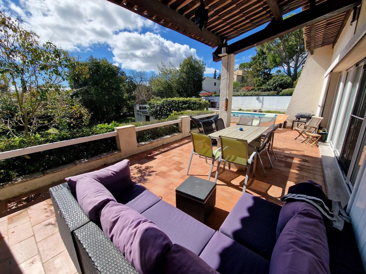 Covered terrace with a purple lounge sofa, dining table with chairs, overlooking the garden and pool