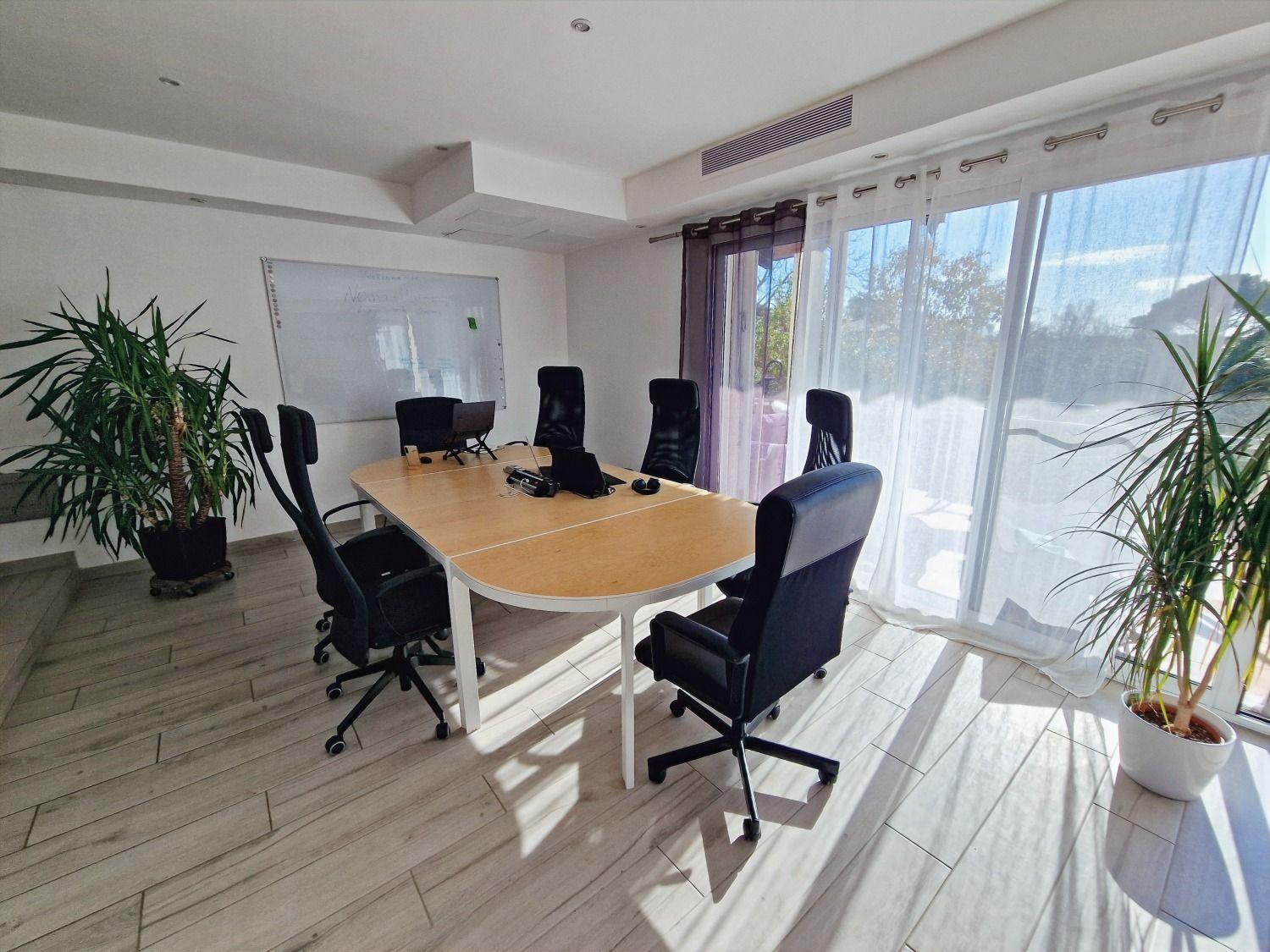 Open-plan coworking space with a large conference table, ergonomic office chairs, whiteboard, and large windows