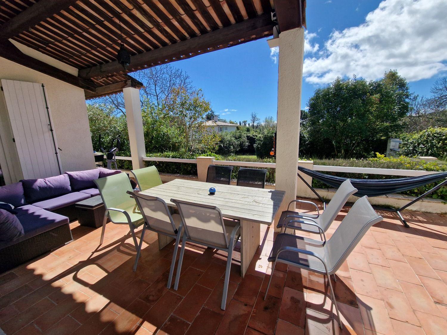 Covered terrace with a large dining table, chairs, and a hammock visible in the garden