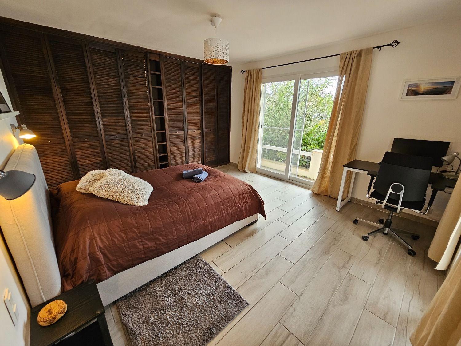 Large bedroom with a double bed, wooden wardrobe, desk, and sliding door to the garden