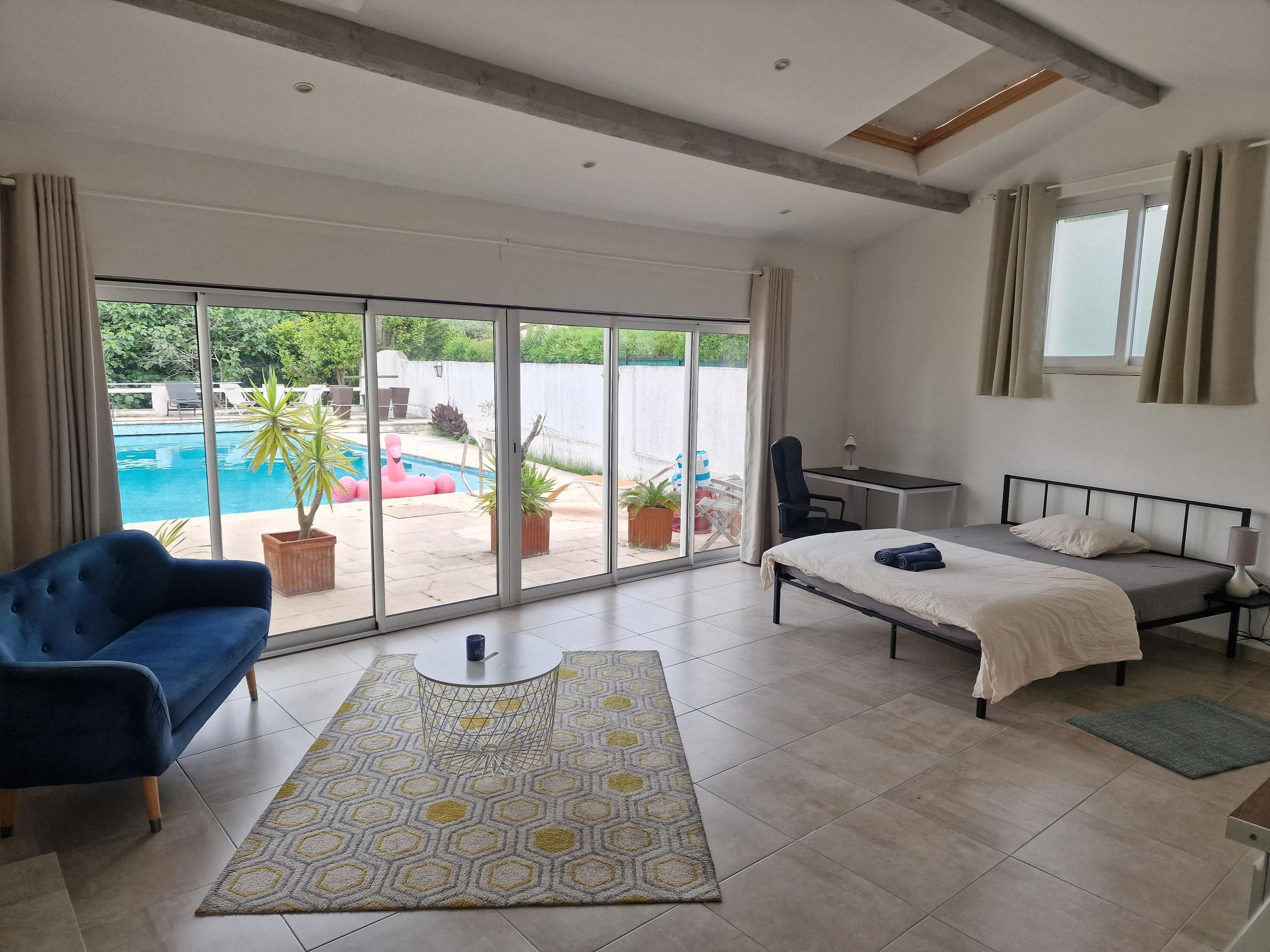 Room Monaco with a large bed, sofa, and floor-to-ceiling sliding doors overlooking the pool