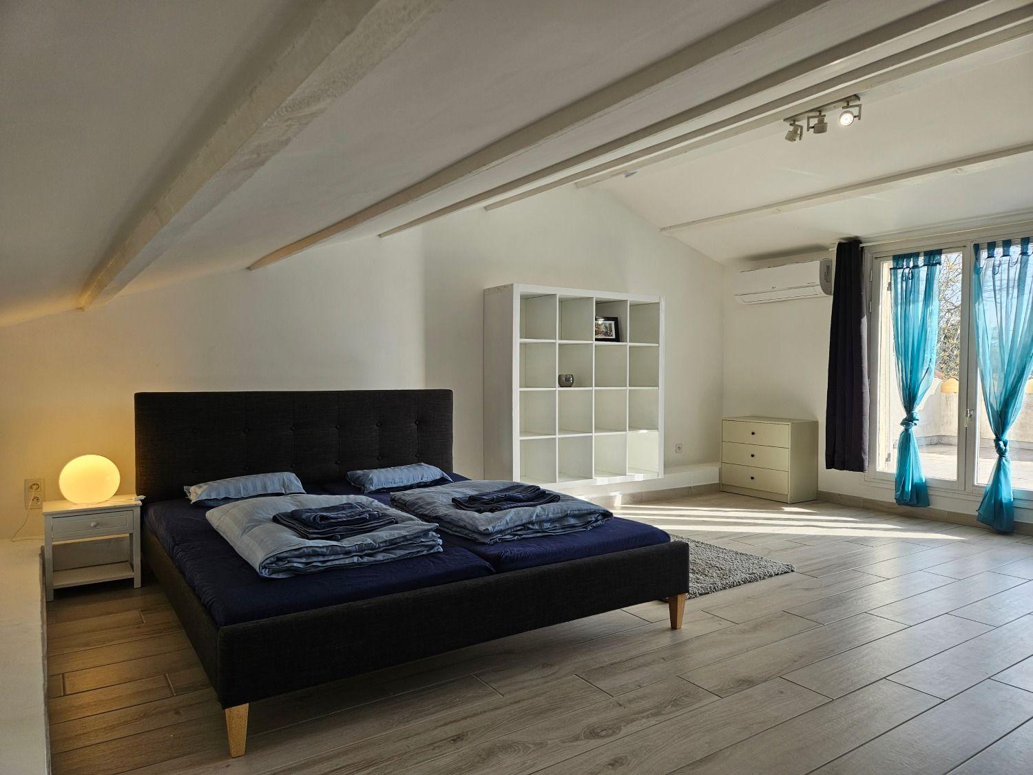 Room Paris attic with a large king-size bed, sloped ceiling, and blue curtains leading to private roof terrace