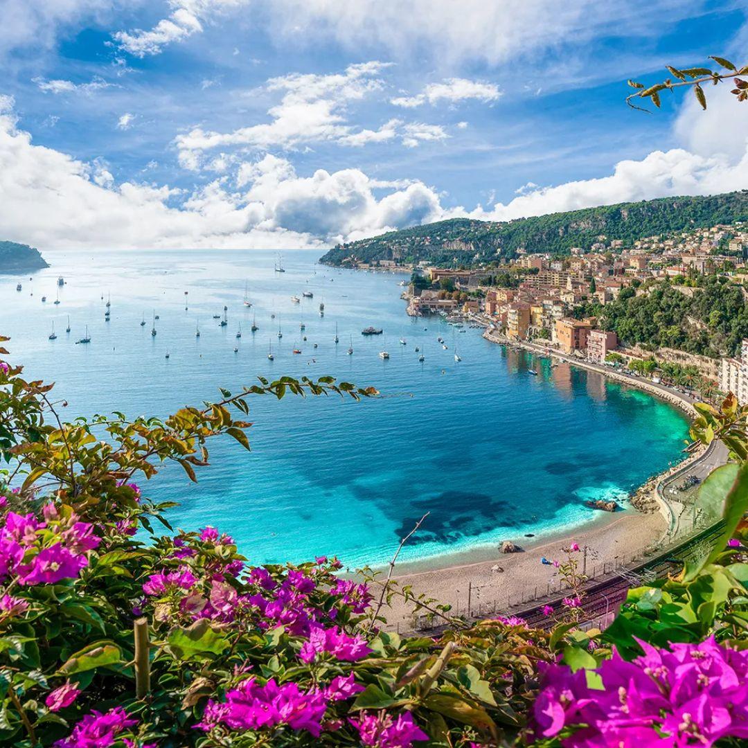 Aerial view of the French Riviera coast at Villefranche-sur-Mer near Nice, with turquoise sea, boats, and bougainvillea flowers