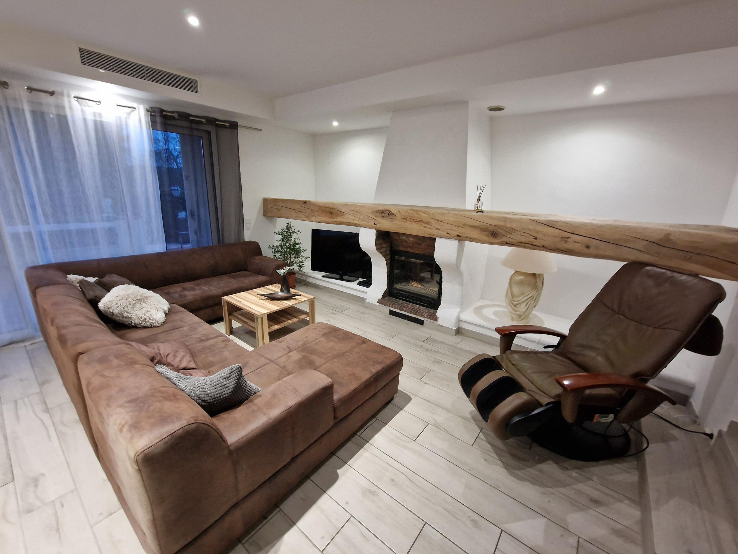 Comfortable living room with a large brown sofa, fireplace, TV, and massage chair