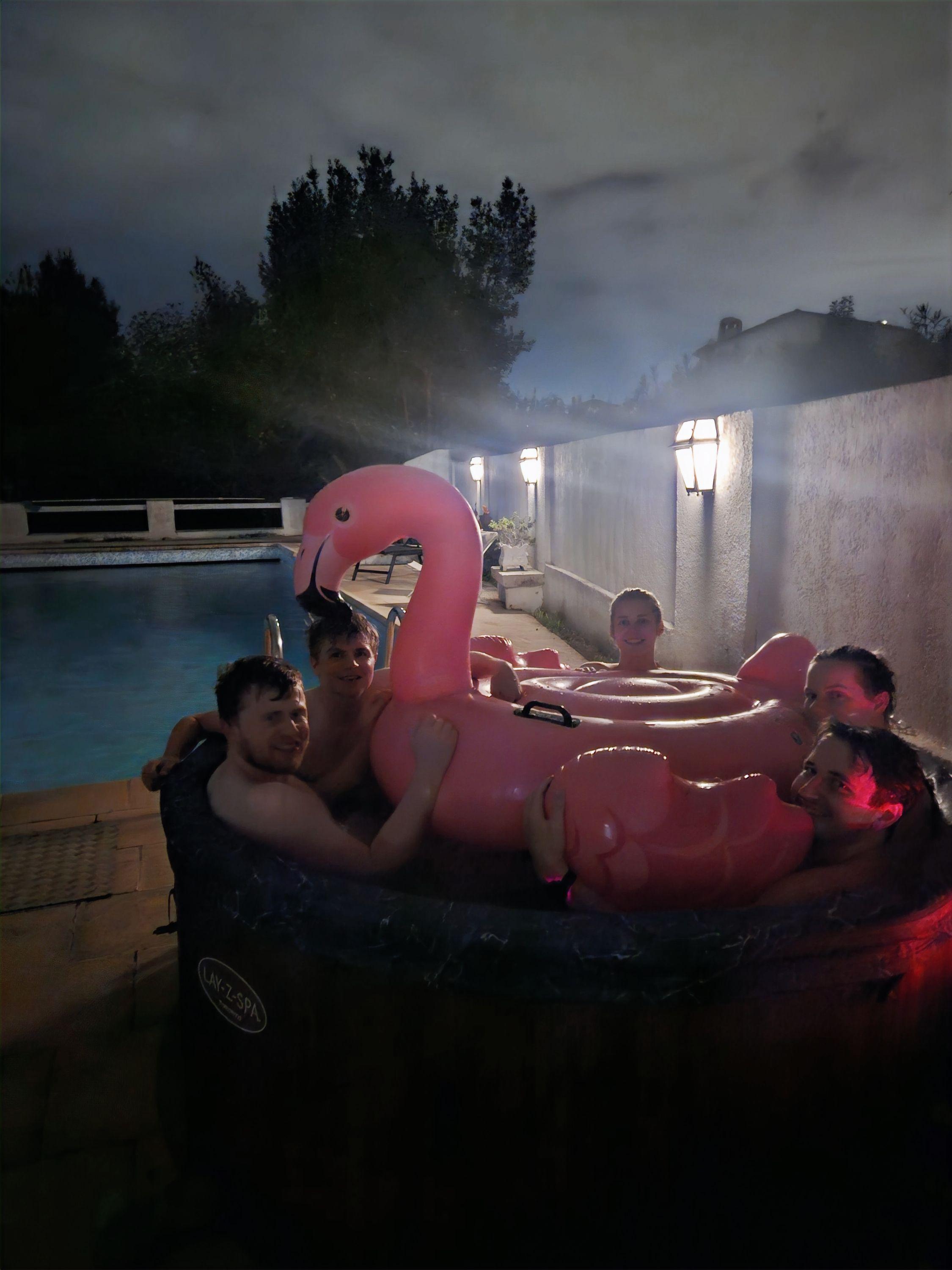 Group of residents relaxing in the jacuzzi at night with a flamingo float