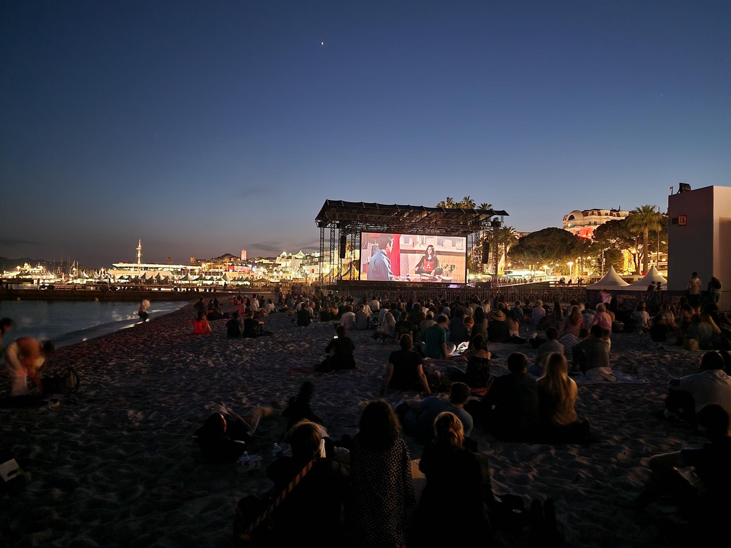 Outdoor cinema screening on the beach at night, likely during the Cannes Film Festival