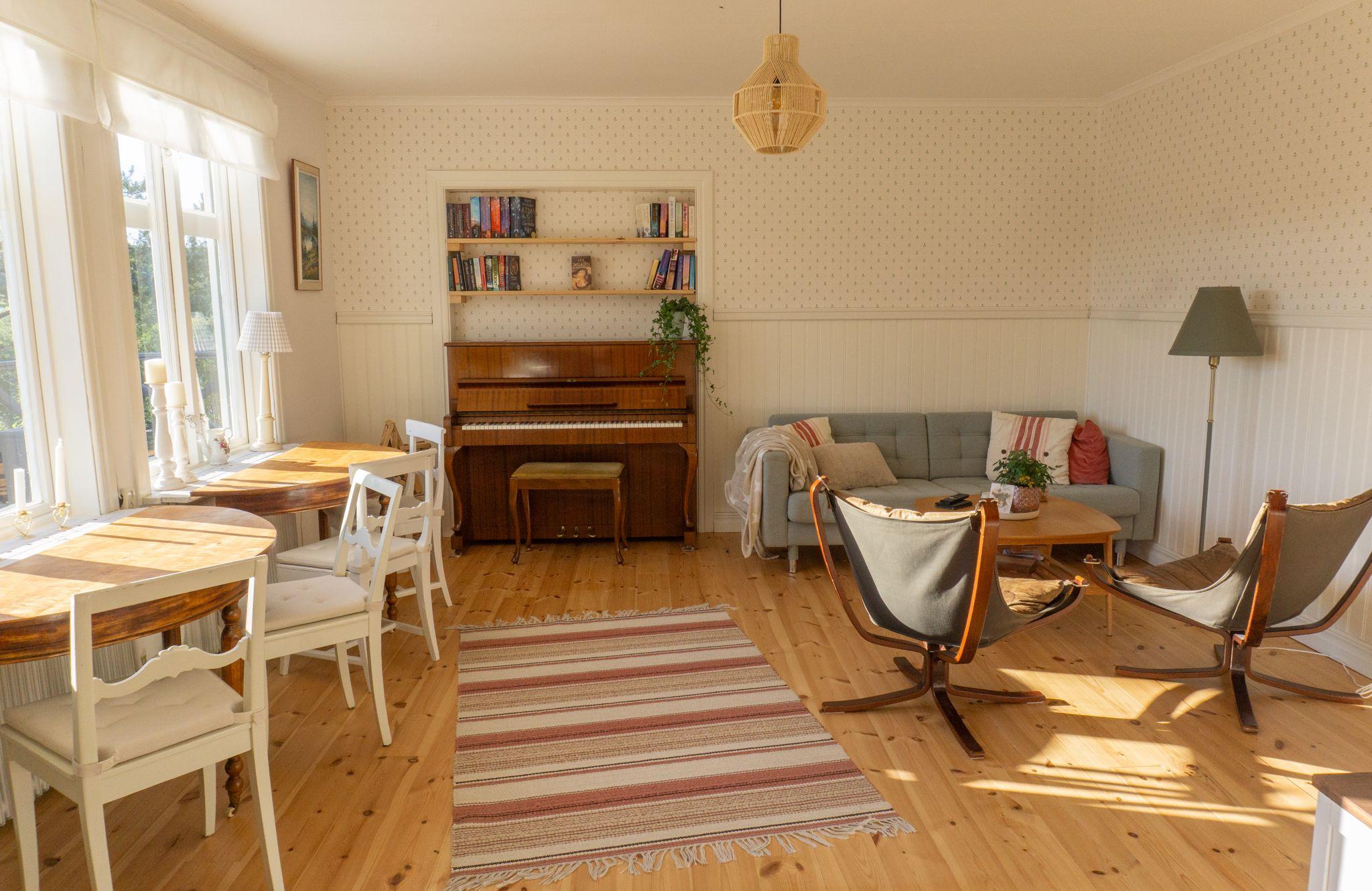 Bright coworking and living room with dining tables, piano, bookshelf and sofa