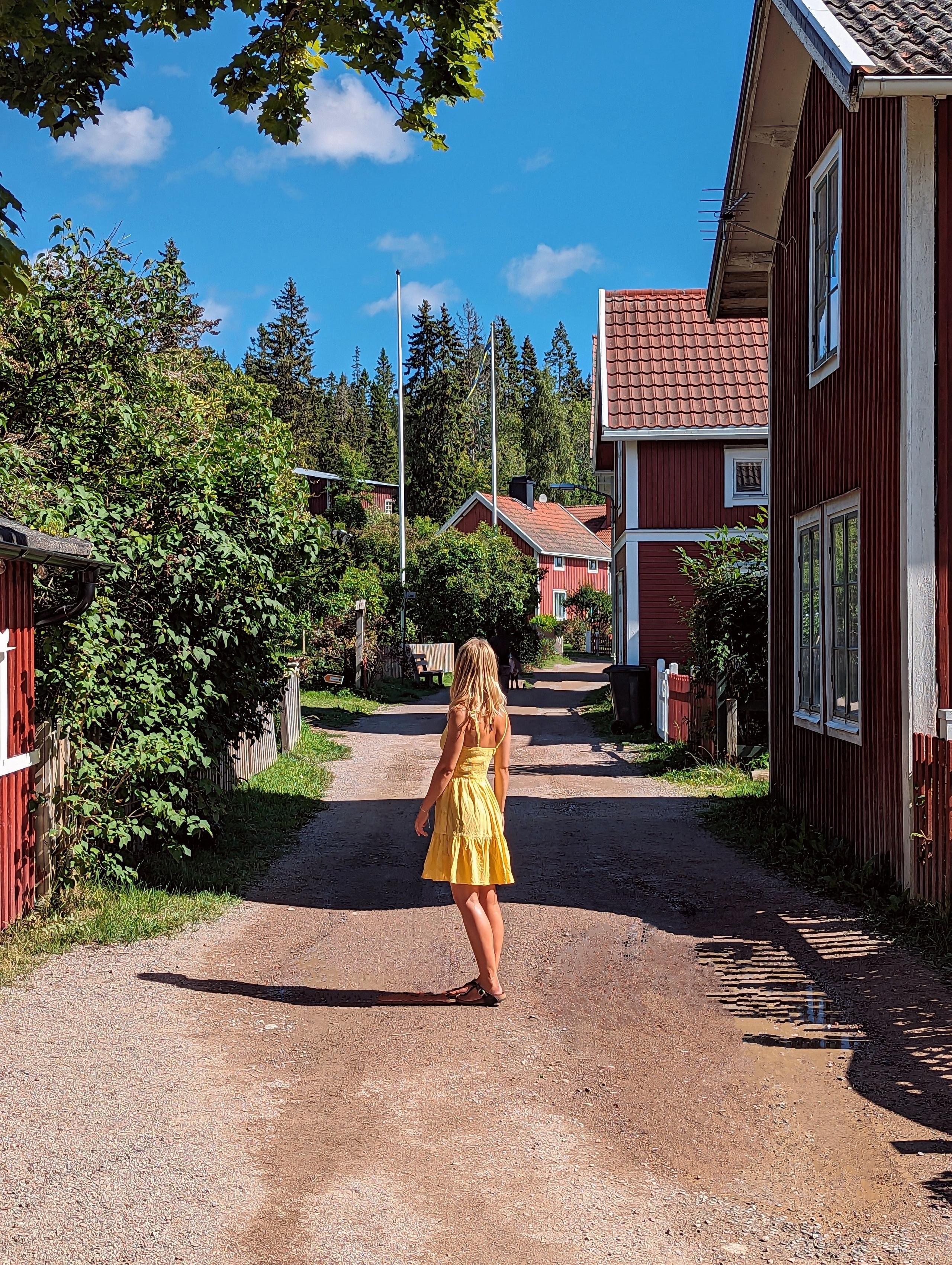 Person in yellow dress walking along a village street lined with red Swedish houses on Ulvön island