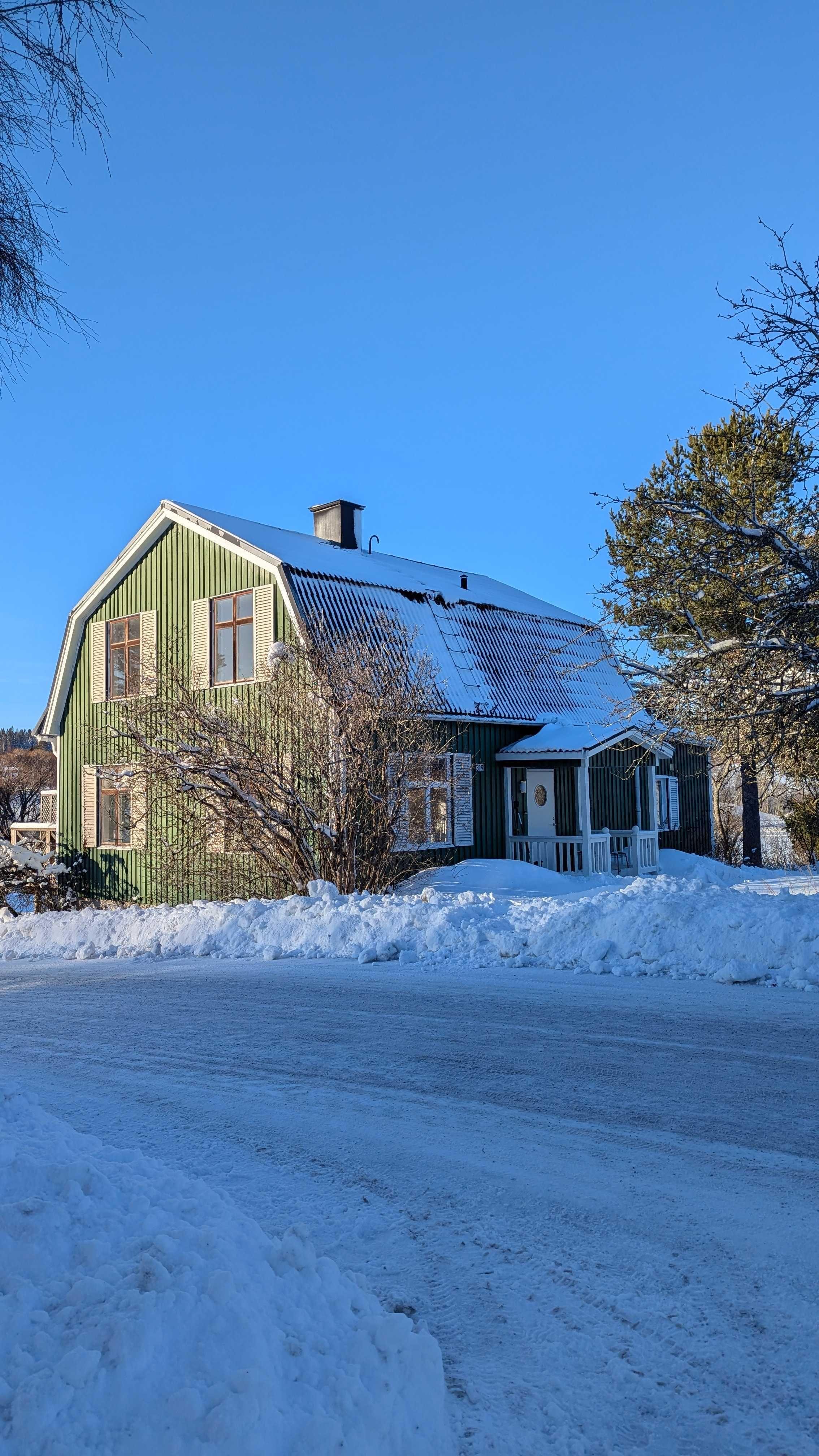 Exterior of the green coliving house covered in snow on a sunny winter day