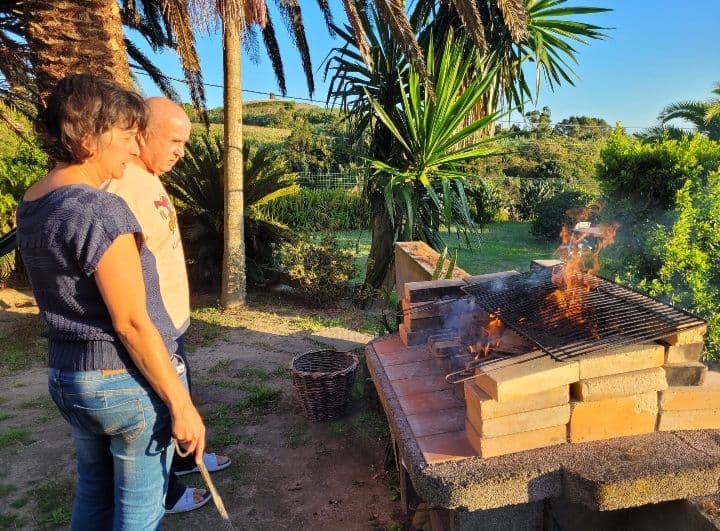 Two people grilling at the outdoor barbecue area with flames visible, surrounded by palm trees and garden