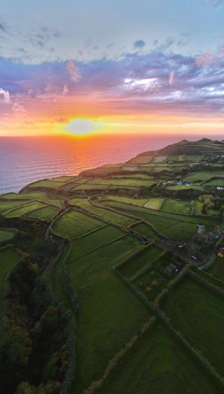 Aerial view of a dramatic sunset over the Atlantic Ocean with green terraced fields of São Miguel island in the foreground