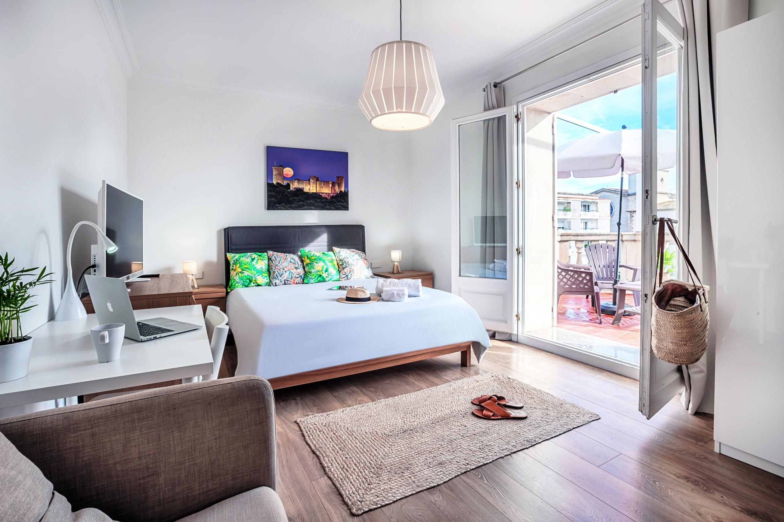 Bright double bedroom with a double bed, private desk with monitor, and open balcony doors leading to a private terrace
