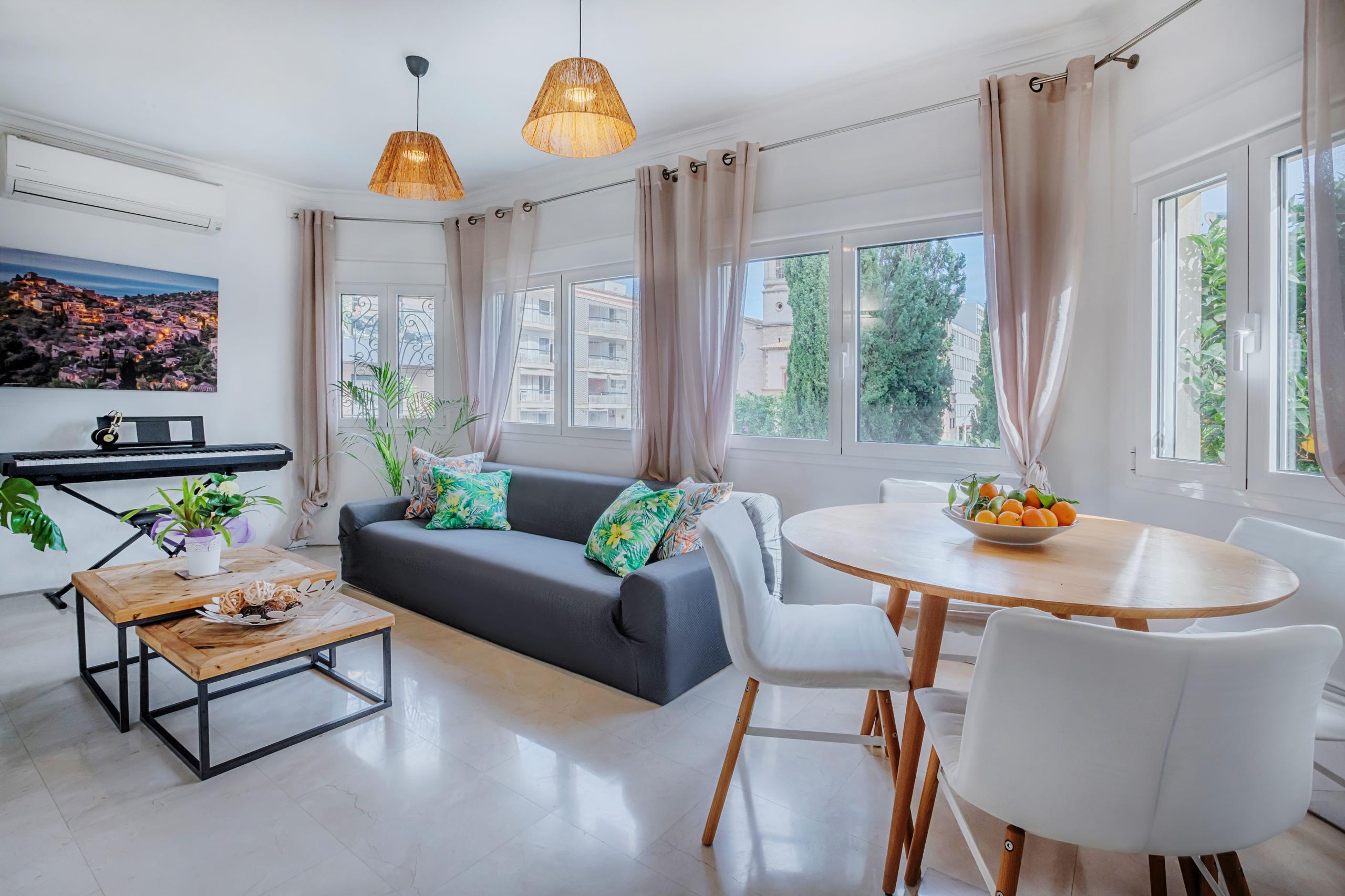 Bright shared lounge and dining area with sofa, round dining table, pendant lights, and large windows overlooking the garden