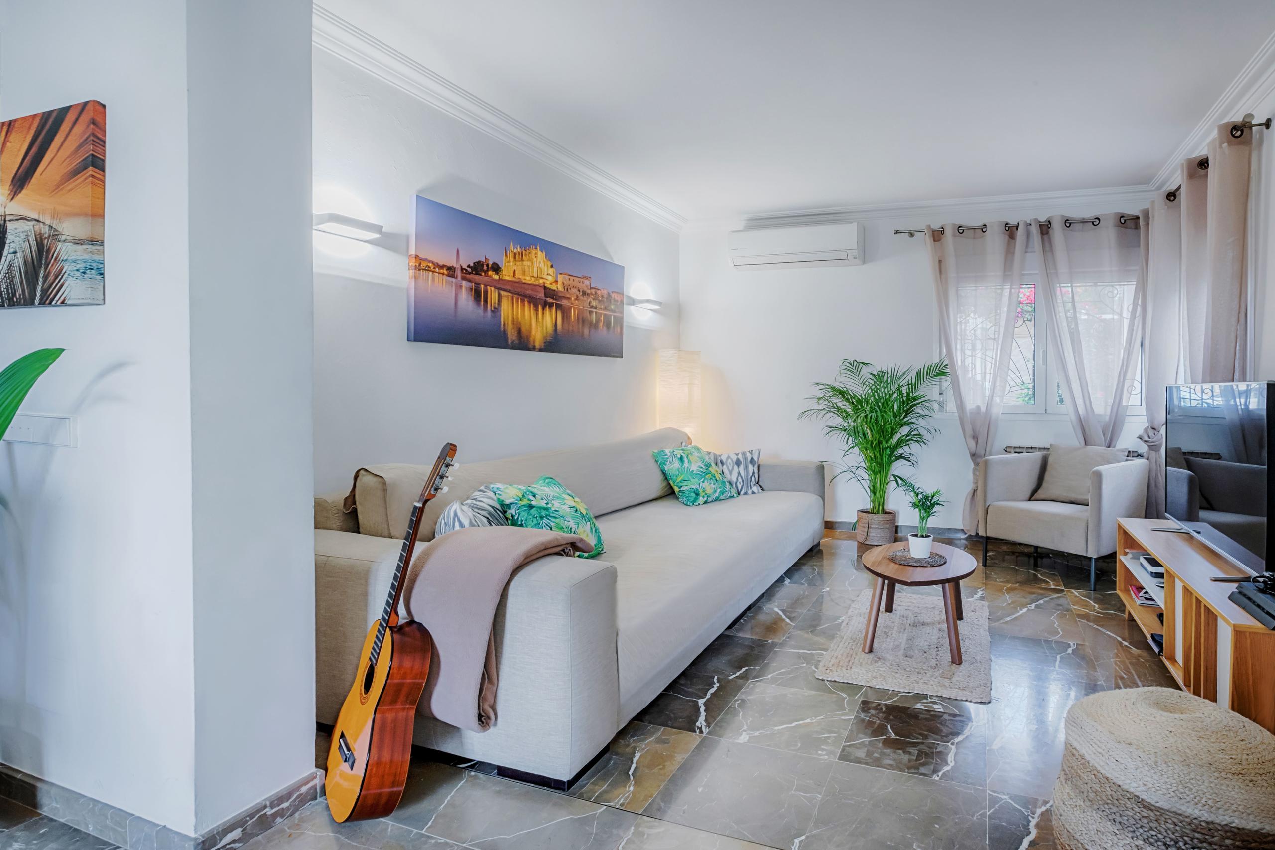 Shared living room with sofa, guitar, armchair, TV, plants, and a large painting of Palma de Mallorca on the wall