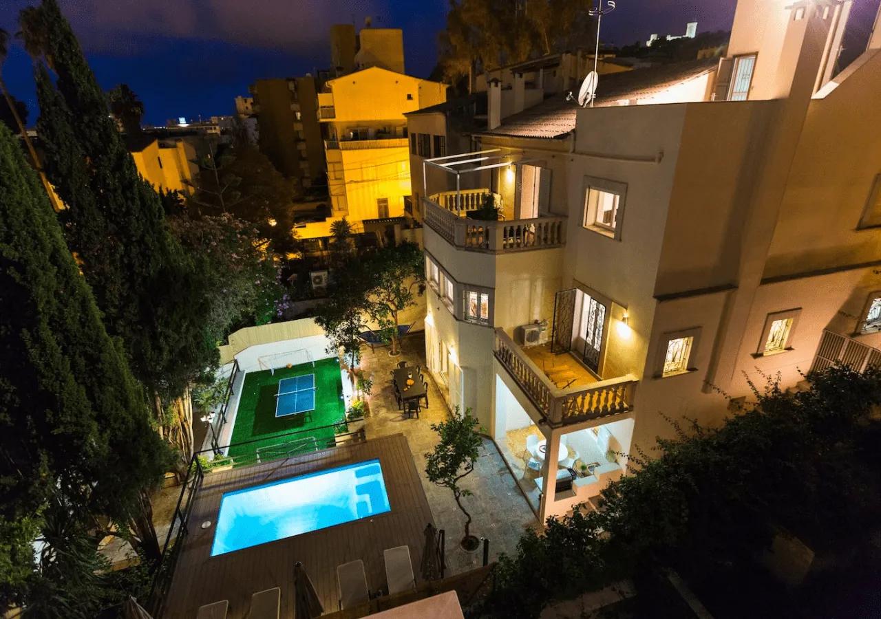 Aerial night view of Villa Armadans showing the illuminated villa building, swimming pool, ping pong table in the garden, and surrounding neighborhood