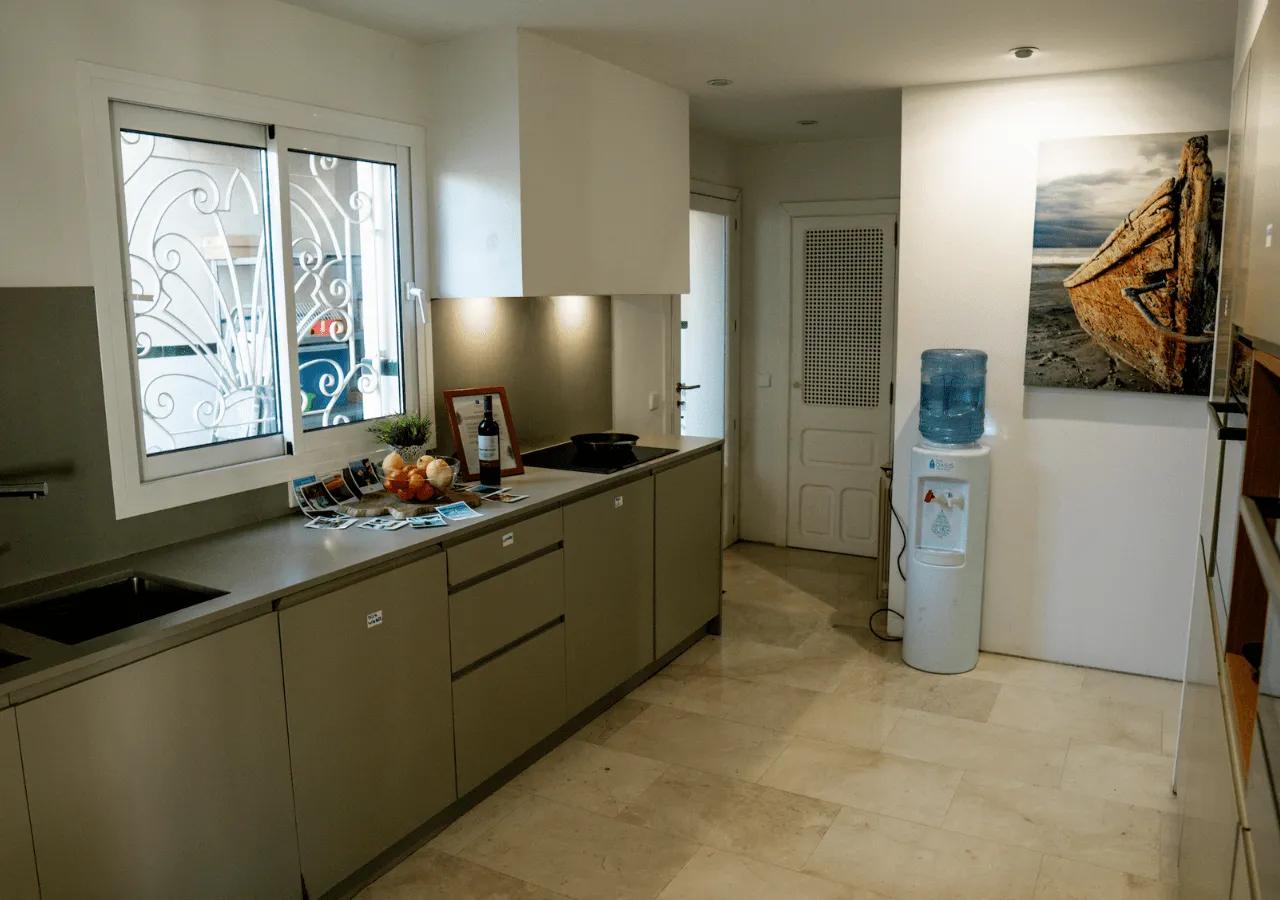 Fully equipped shared kitchen with modern countertops, induction hob, water dispenser, and artwork on the wall