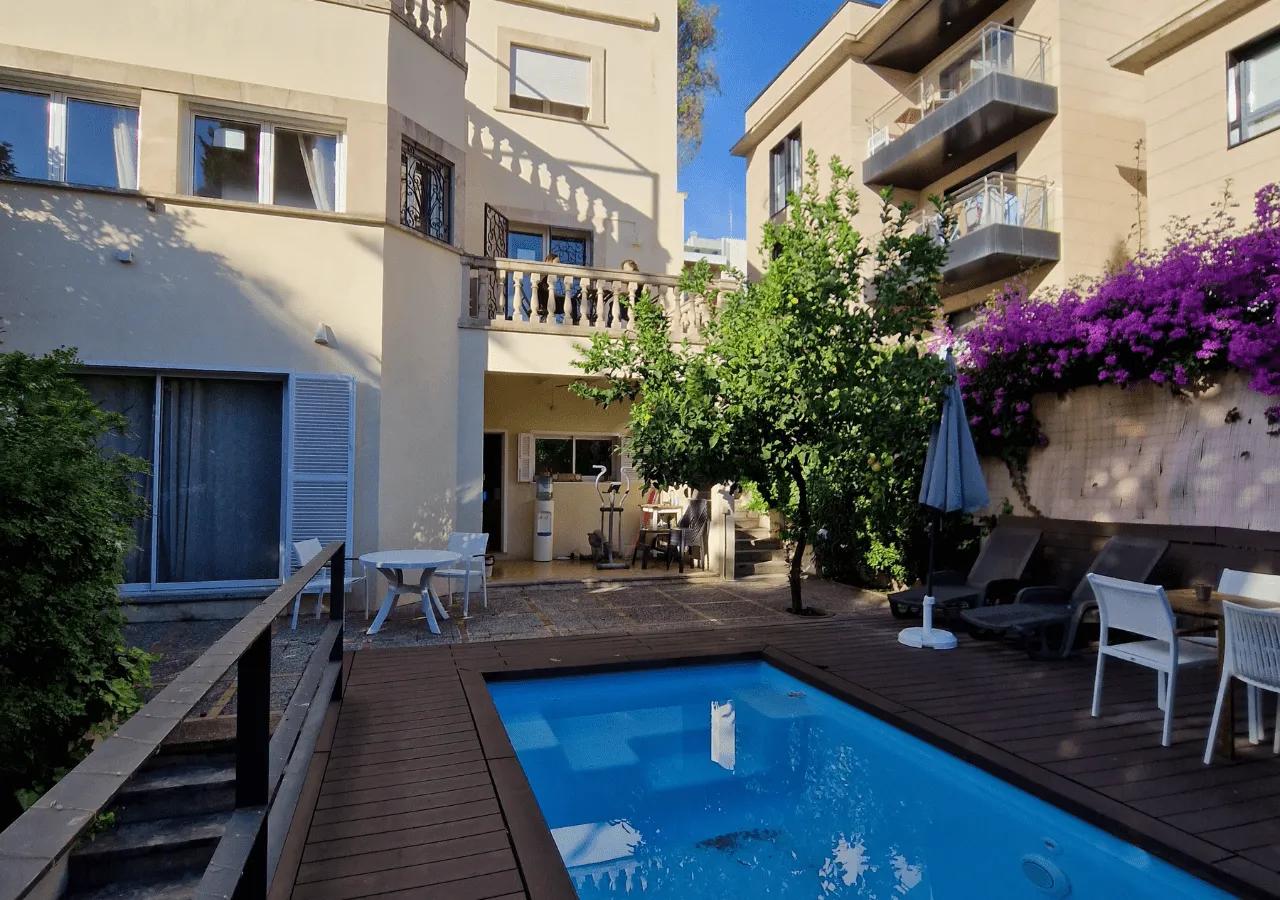 Garden view showing the swimming pool, wooden deck, sun loungers, and purple bougainvillea flowers on the villa wall