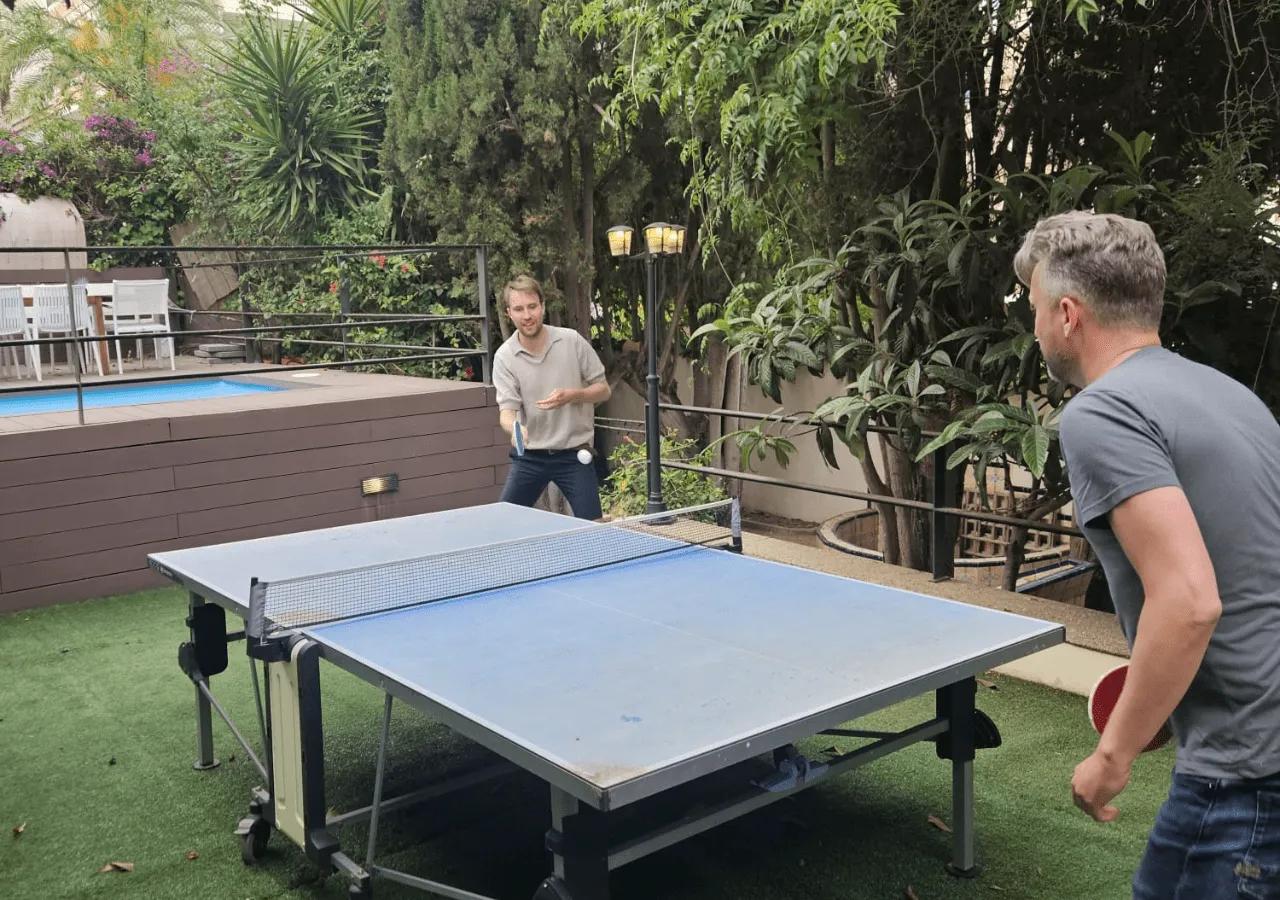 Two residents playing table tennis in the garden area next to the swimming pool