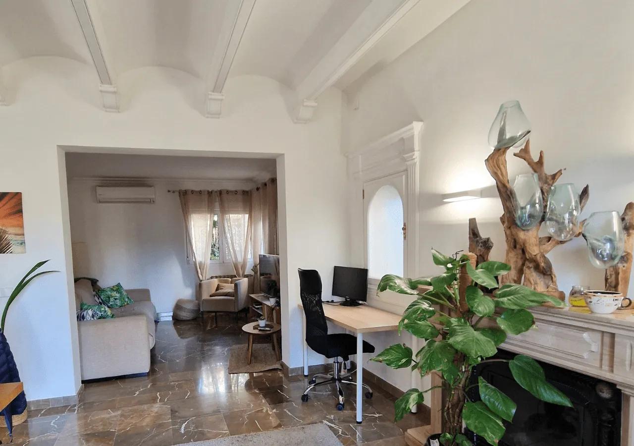 View of the coworking area with a desk and chair, connected to the lounge area with sofas and plants