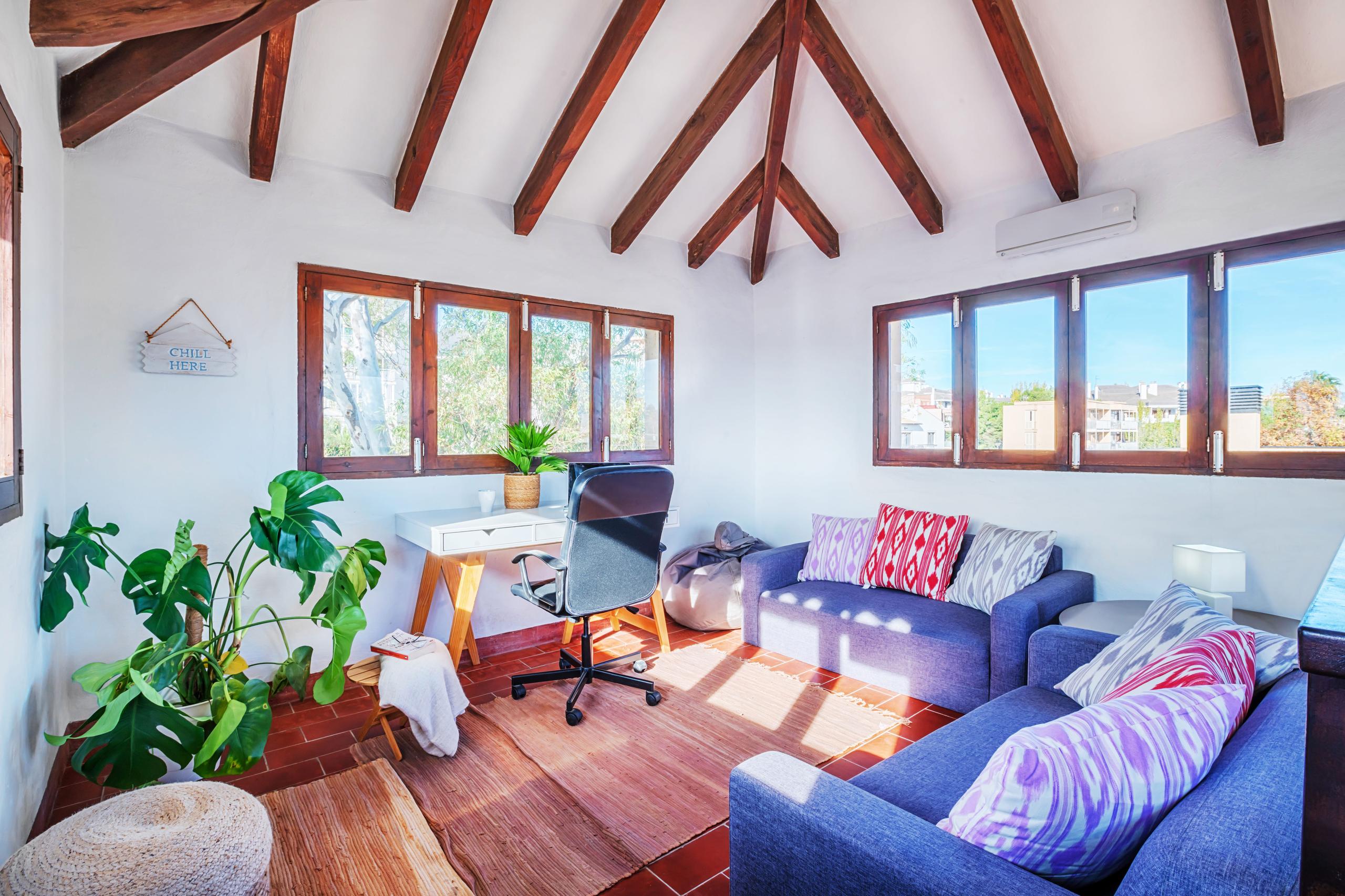 Top floor call room with wooden beamed ceiling, desk, chair, blue sofas, and panoramic windows with views of the surroundings