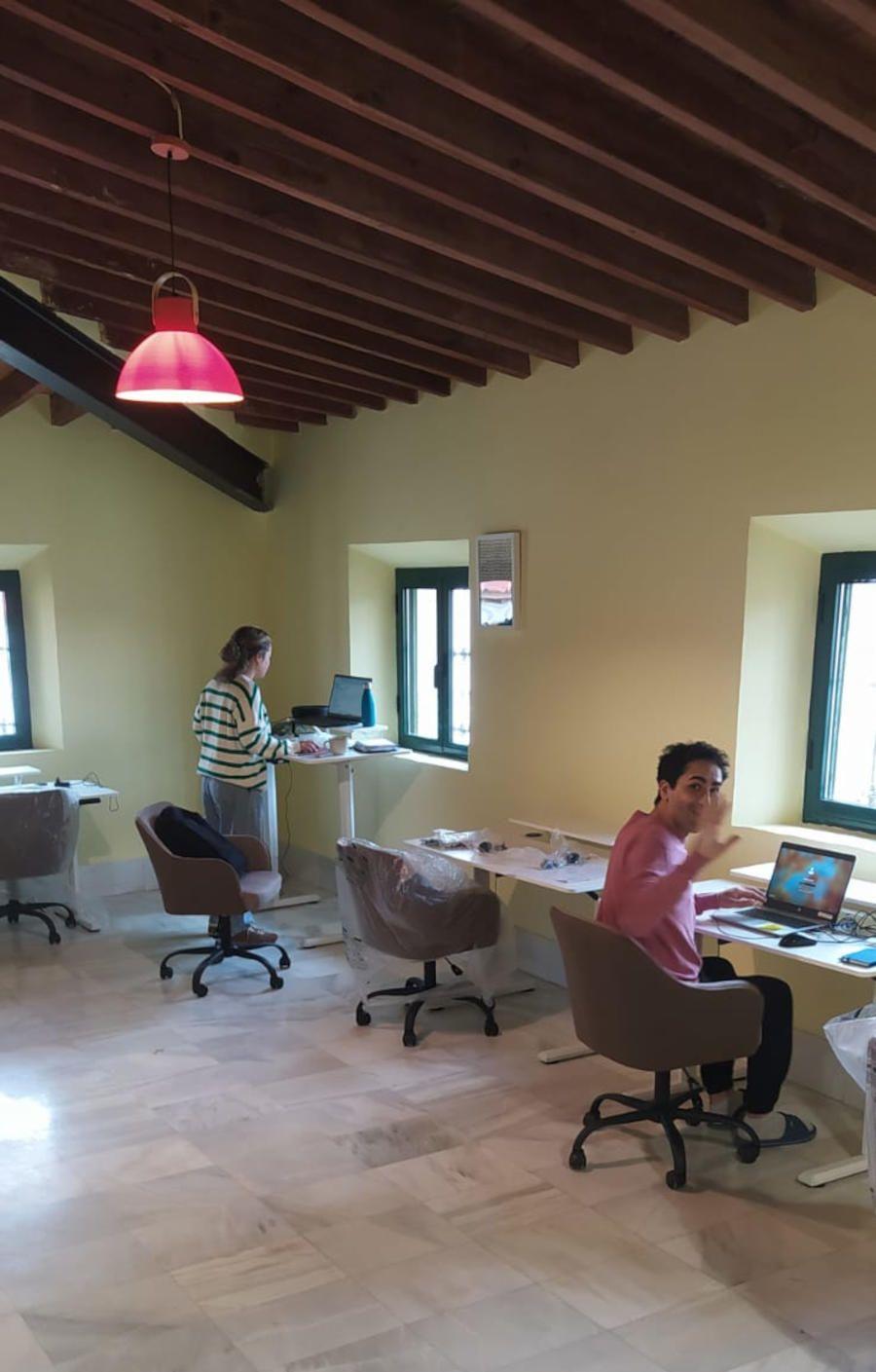 Wide view of the attic coworking space with standing desks, ergonomic chairs, wooden beam ceiling and multiple windows