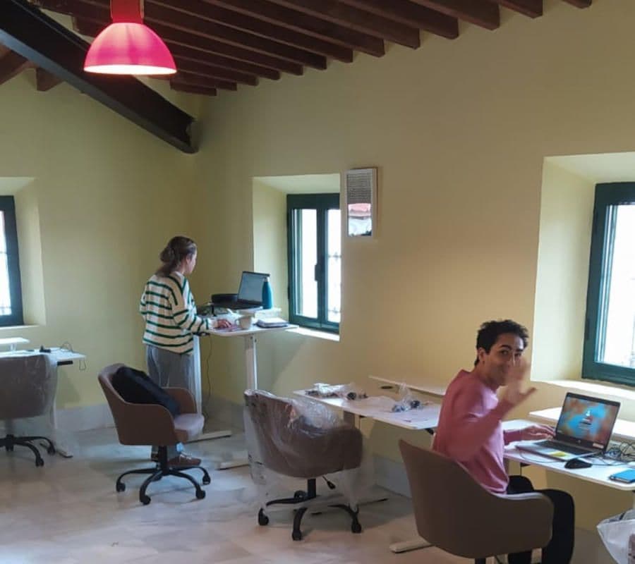 Two people working in the attic coworking space with standing desks, ergonomic chairs, wooden beam ceiling and green-framed windows