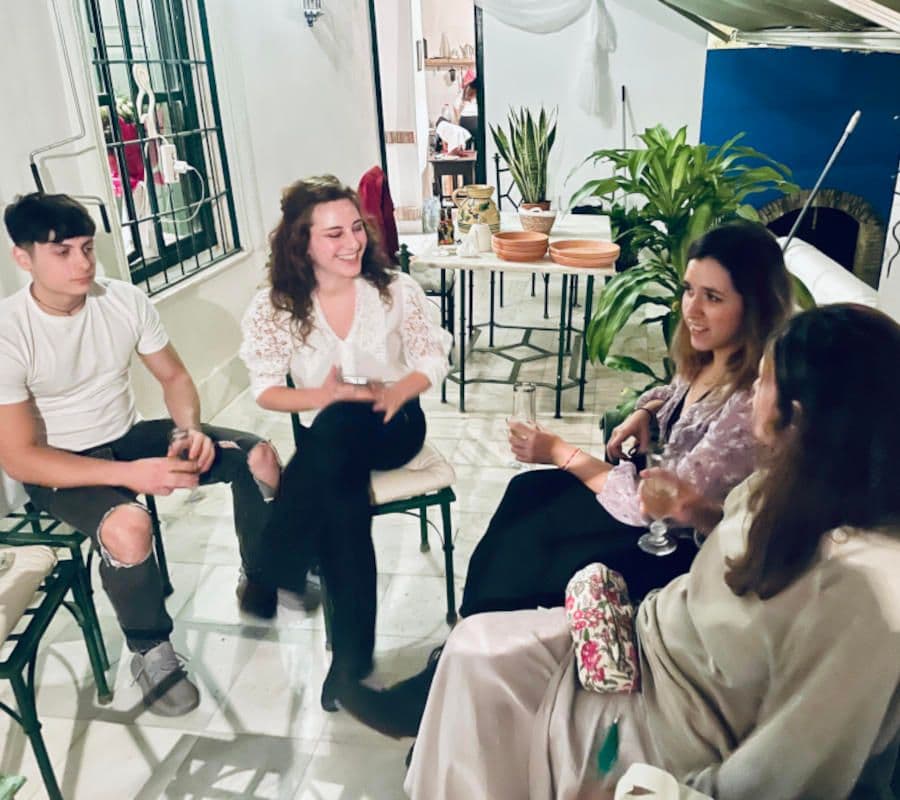 Four people sitting in a circle chatting and laughing in the patio area, surrounded by plants