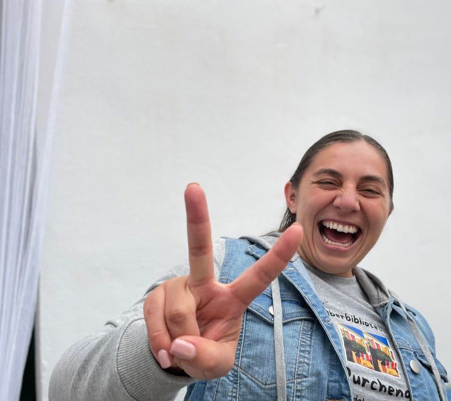 A smiling woman making a peace sign, wearing a Purchena badge, at the Iberbibliotecas event