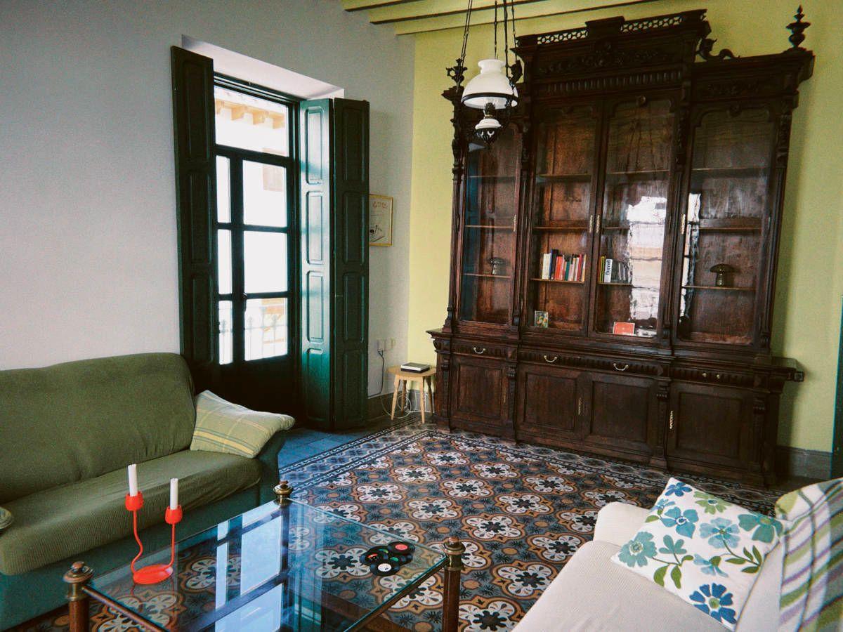 The living room with green sofas, a large antique wooden bookcase, colourful mosaic tile floor and tall green shuttered windows