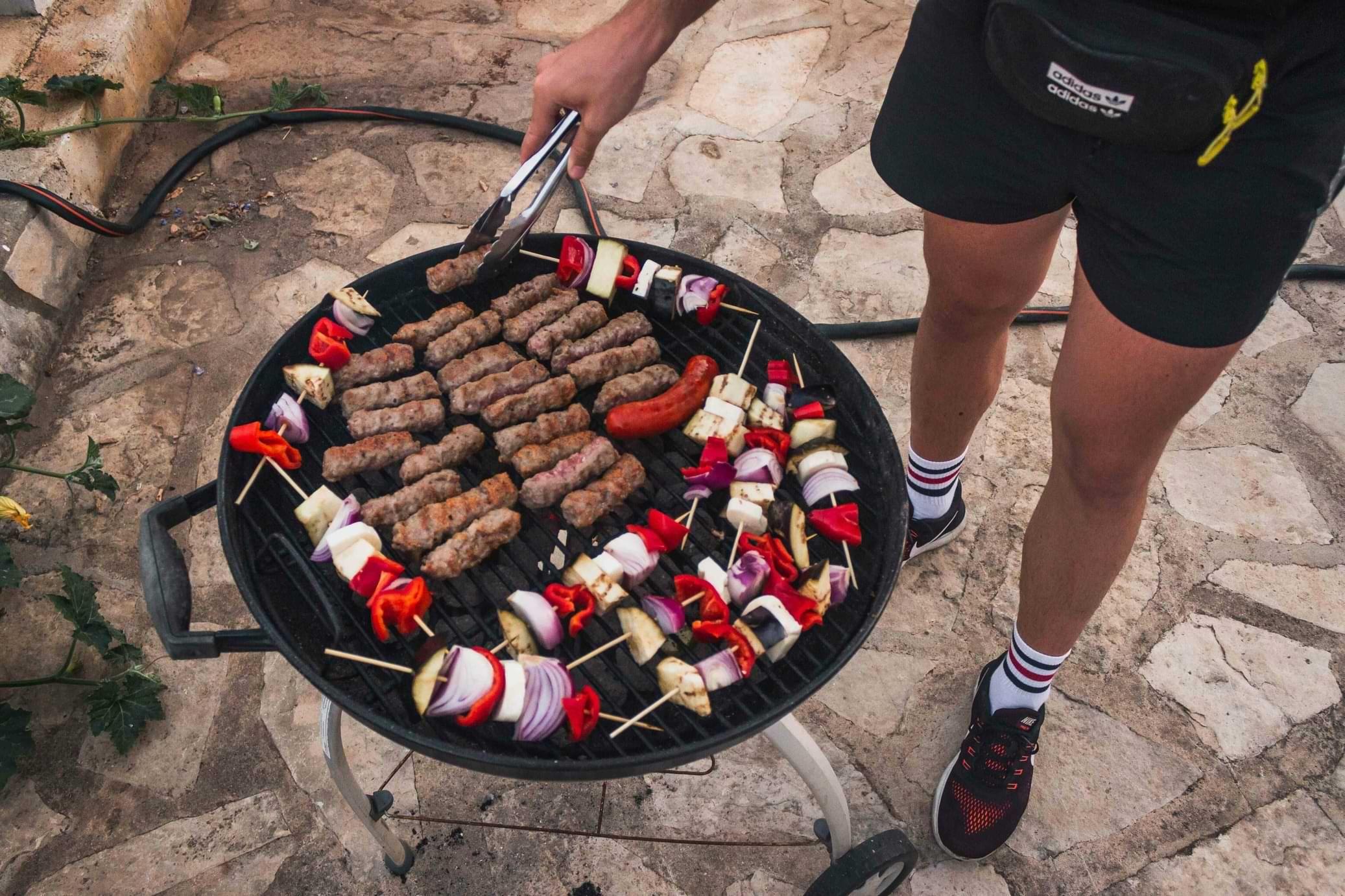 Person grilling meat and vegetable skewers on a BBQ in the garden area