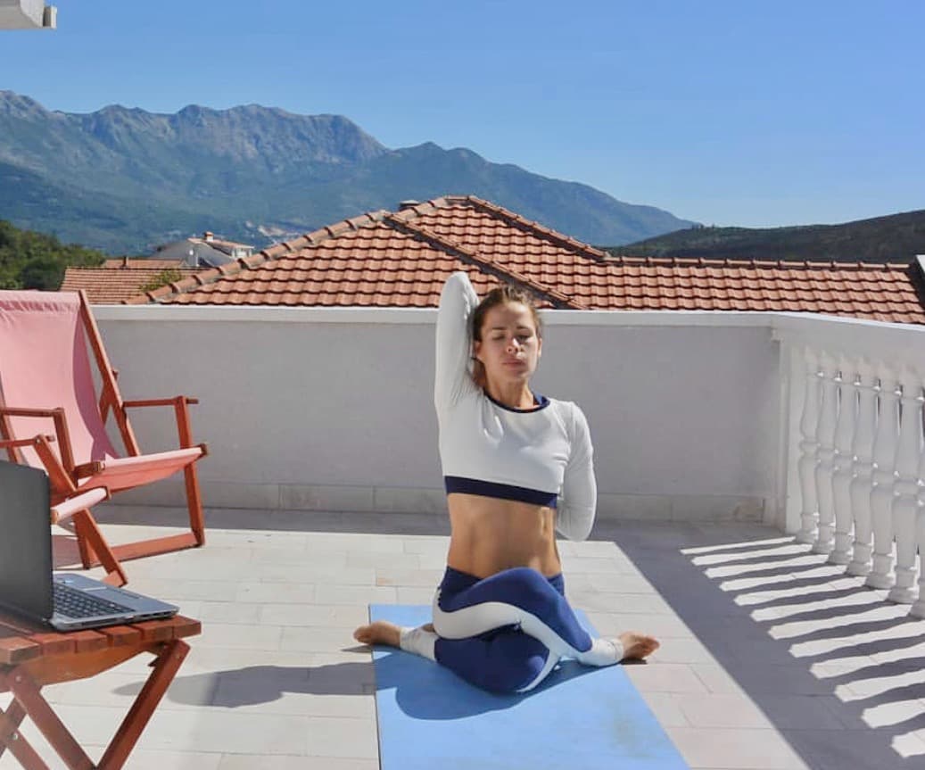 Person doing yoga on the rooftop terrace with mountain views in the background