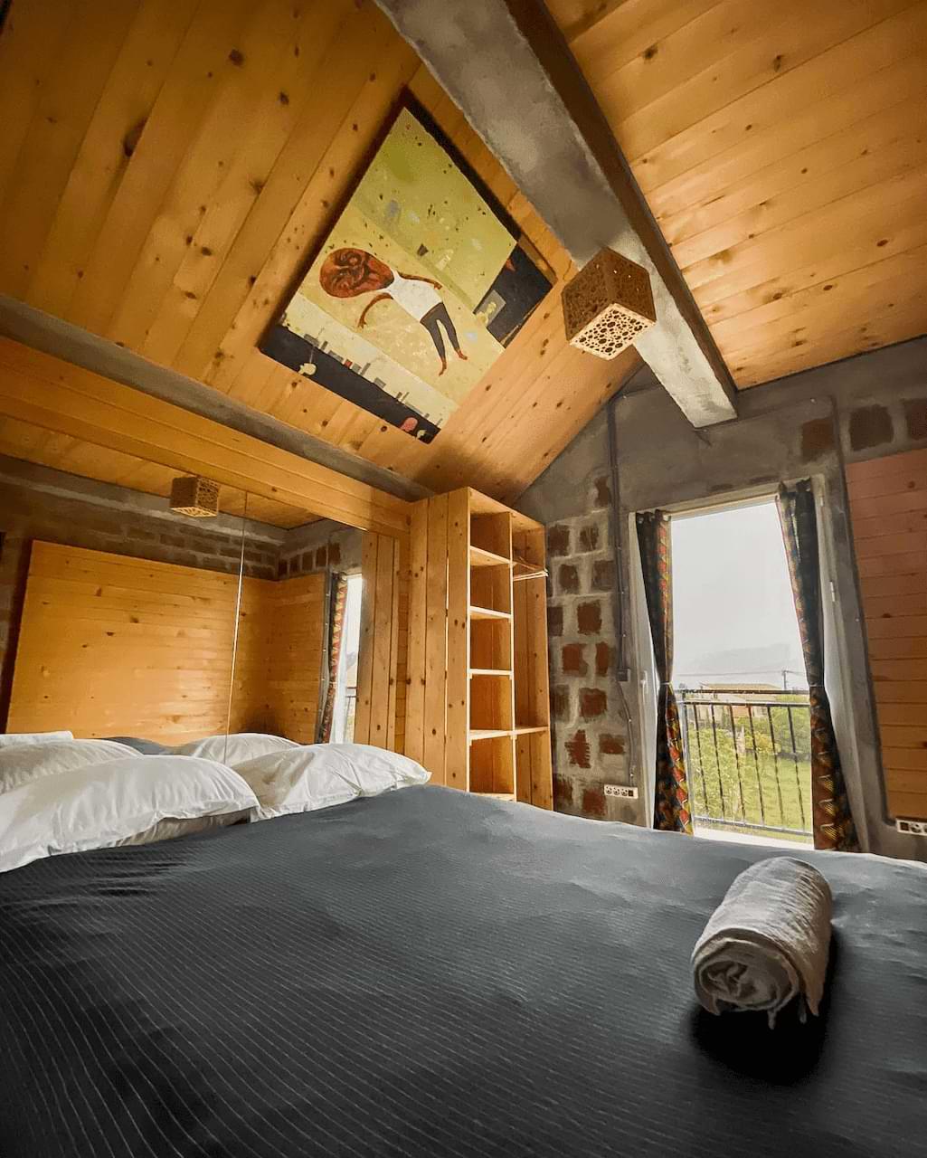 Premium private room with a double bed, wooden ceiling, shelving, and a balcony door