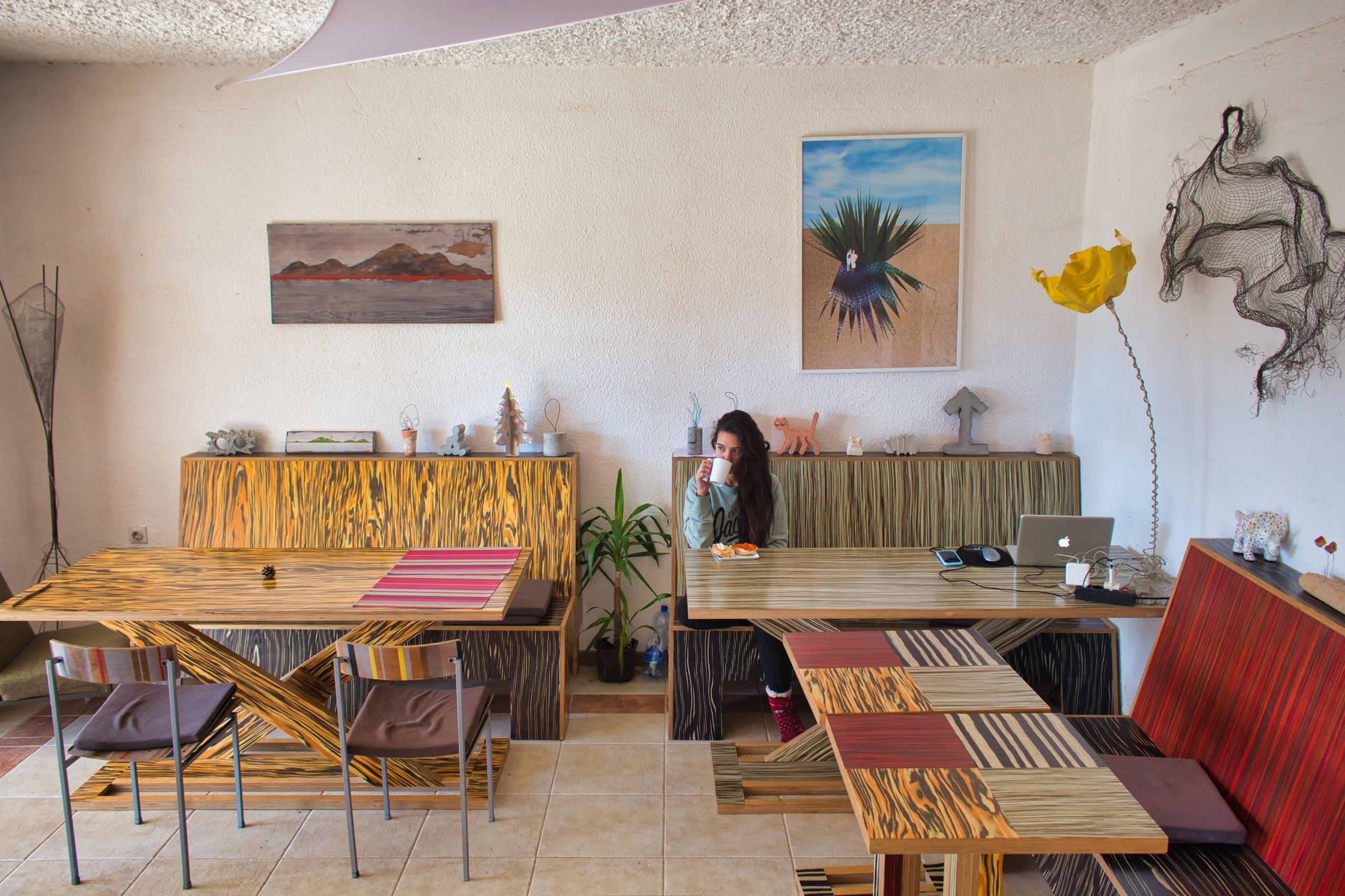 Spacious living room with colorful wooden furniture, artwork on walls, and a resident working on a laptop