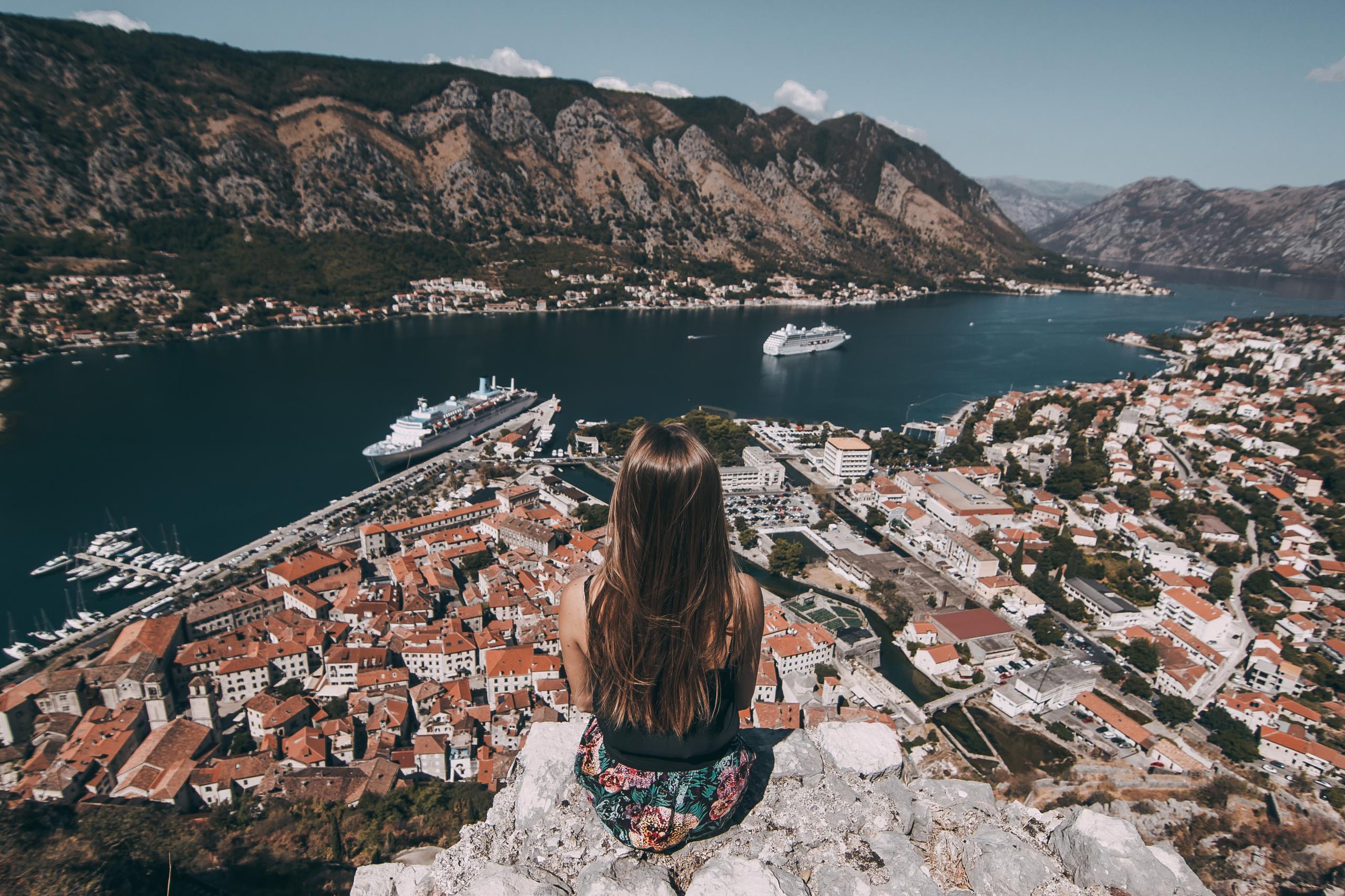 Woman sitting on a cliff overlooking Kotor Bay with cruise ships and mountains