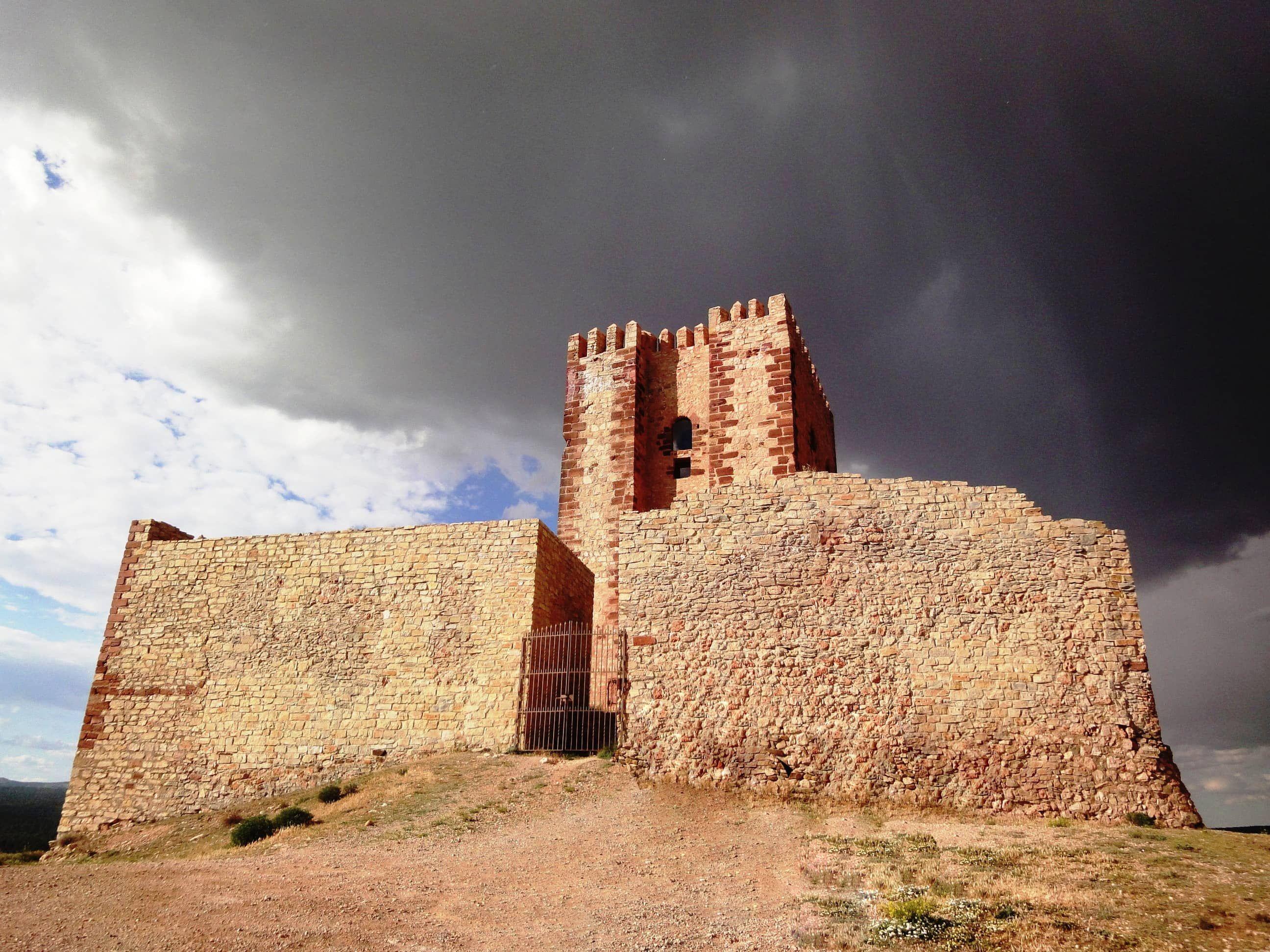 Medieval stone castle with dark cloudy sky and arid terrain in Molina de Aragón