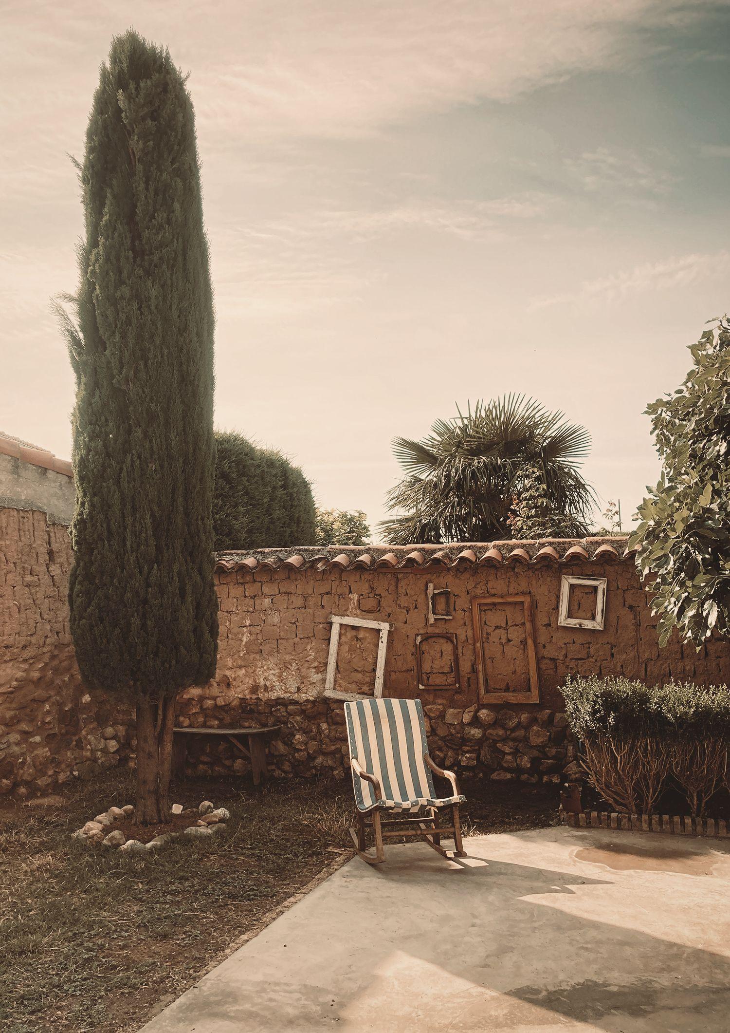 Garden at Posada de la Luz with a rocking chair, several antique wooden frames hanging on an adobe wall, and a tree