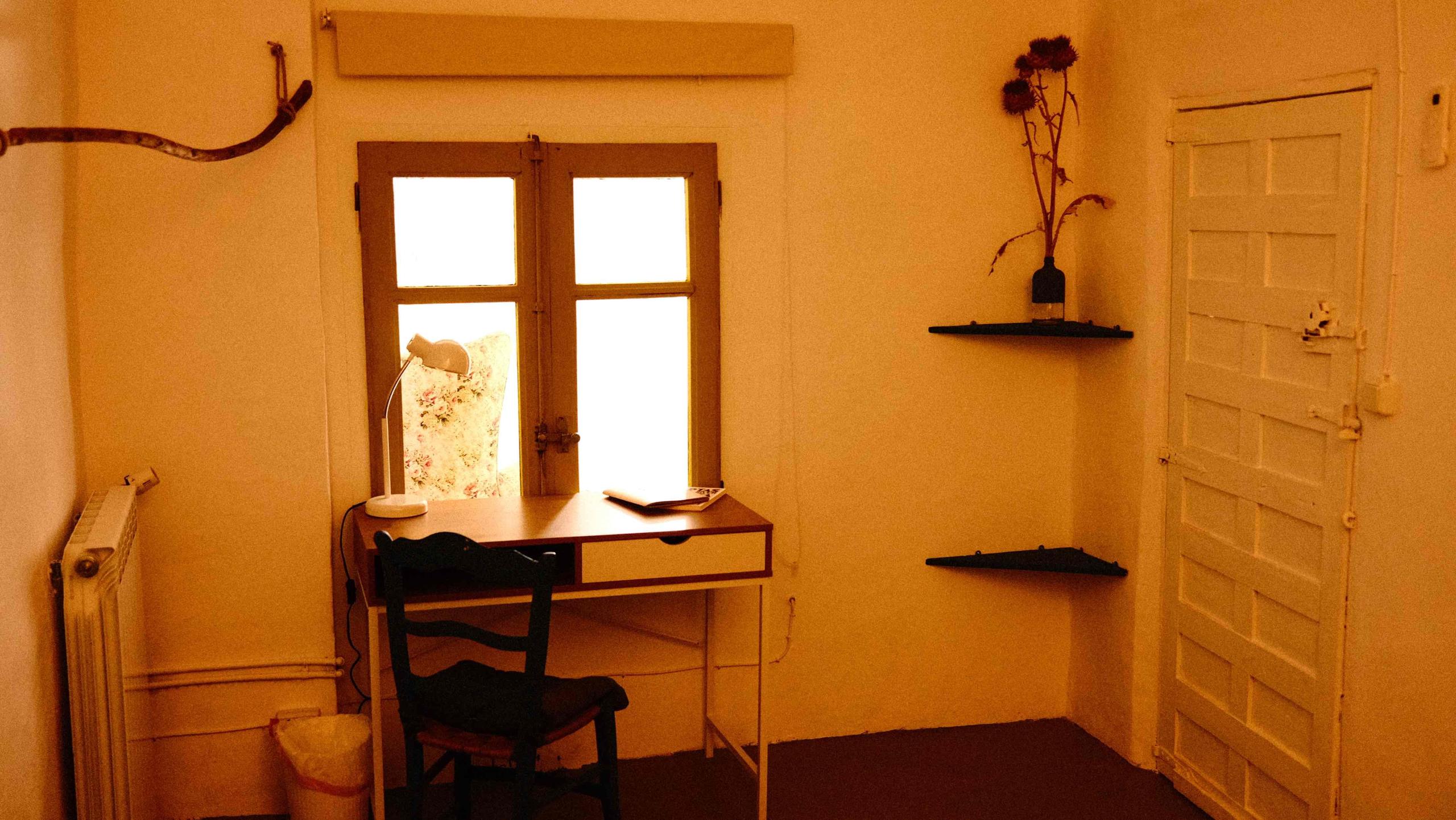 The Woodman room showing an interior window, study desk, lamp, chair, open books, dried flowers, corner shelves and connectivity cube