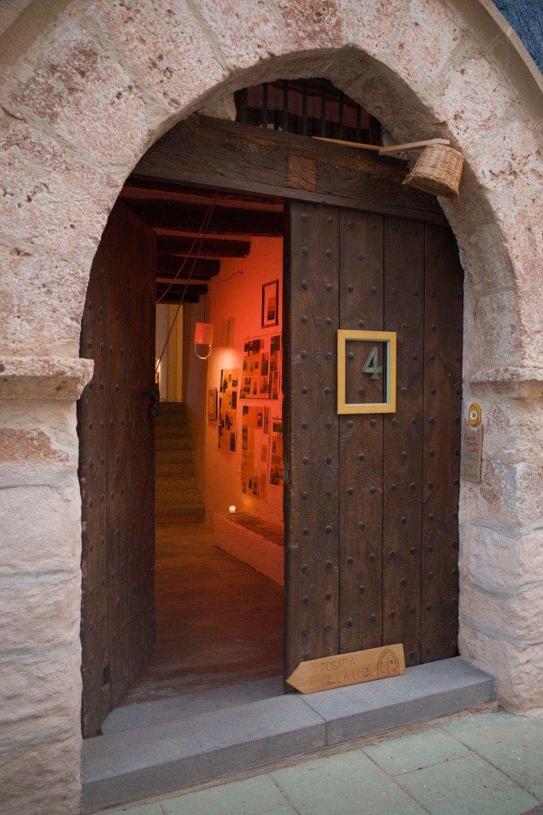 Antique wooden entrance door to Posada de la Luz with the number 4 and an exhibition by Juanan Requena visible inside