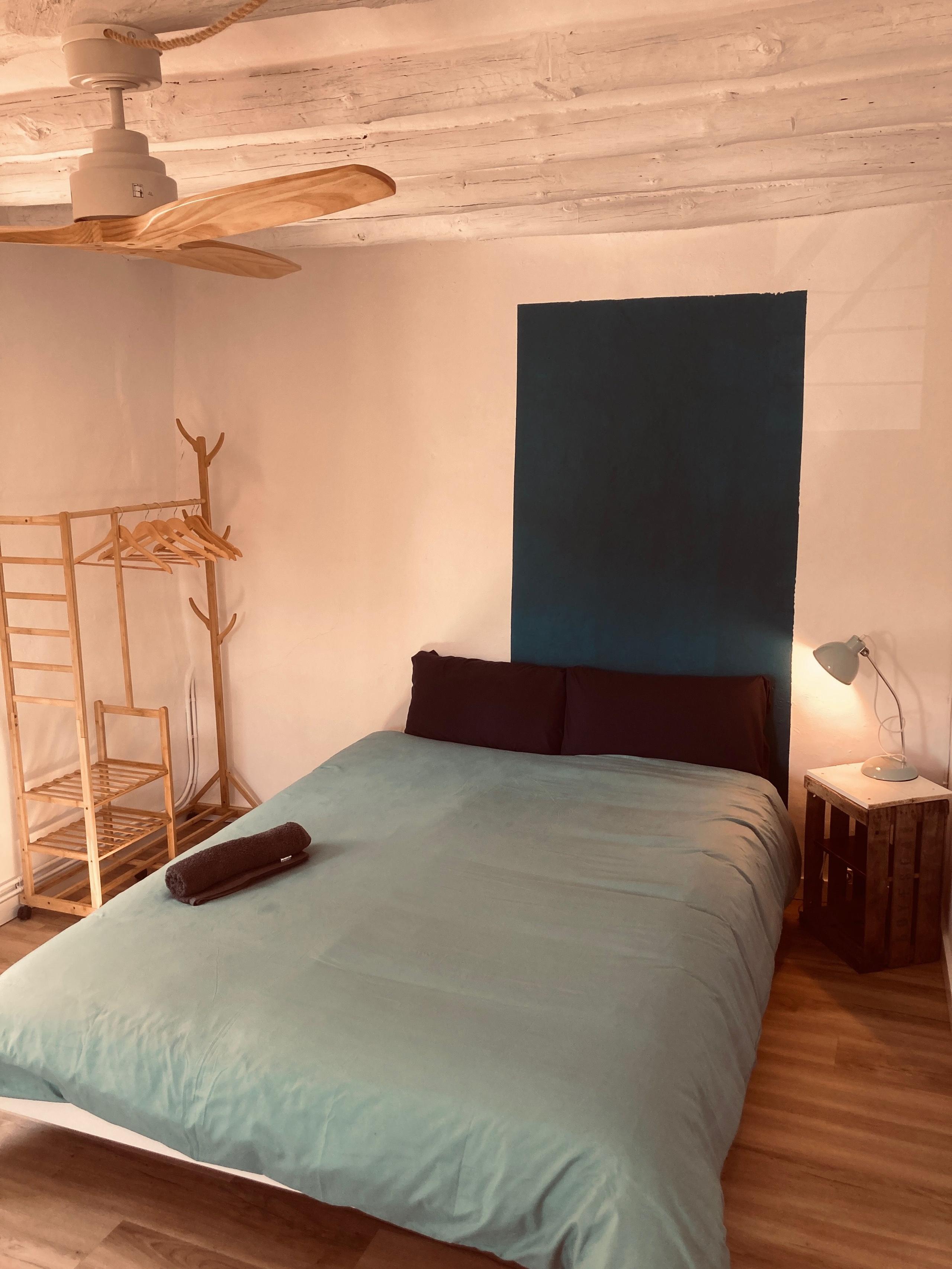 Bed, nightstand with lamp, fan and open wardrobe in La Rinko room