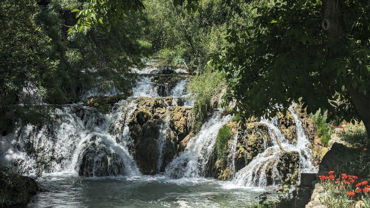 Waterfall on rocks with water flowing over stones and green trees around the Río Mesa