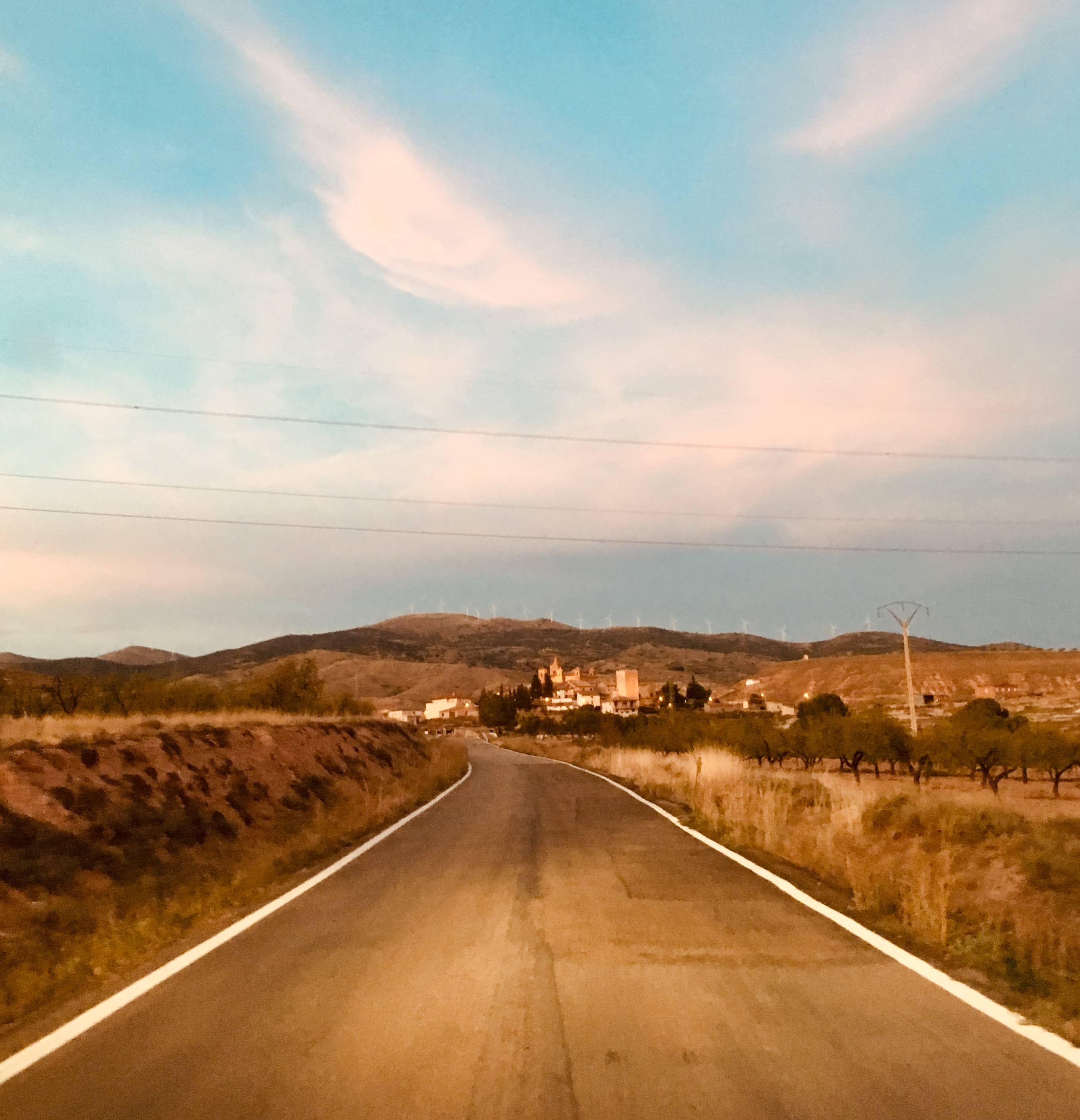 Road leading to a village, mountains and blue sky with clouds, surroundings of Posada de la Luz