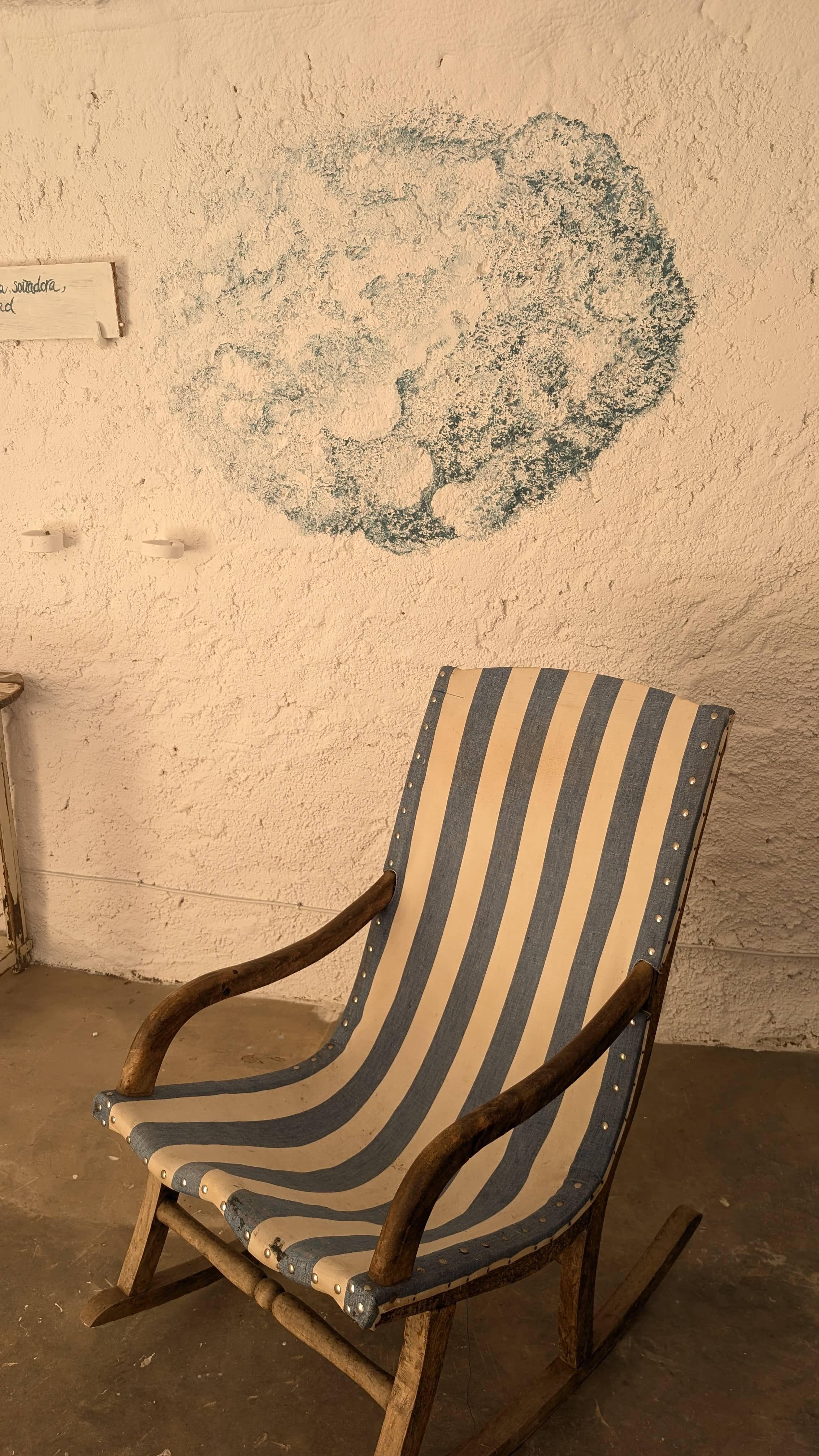 Wall of the Posada de la Luz workshop with a cloud and a phrase painted by María José and a rocking chair with blue and white stripes