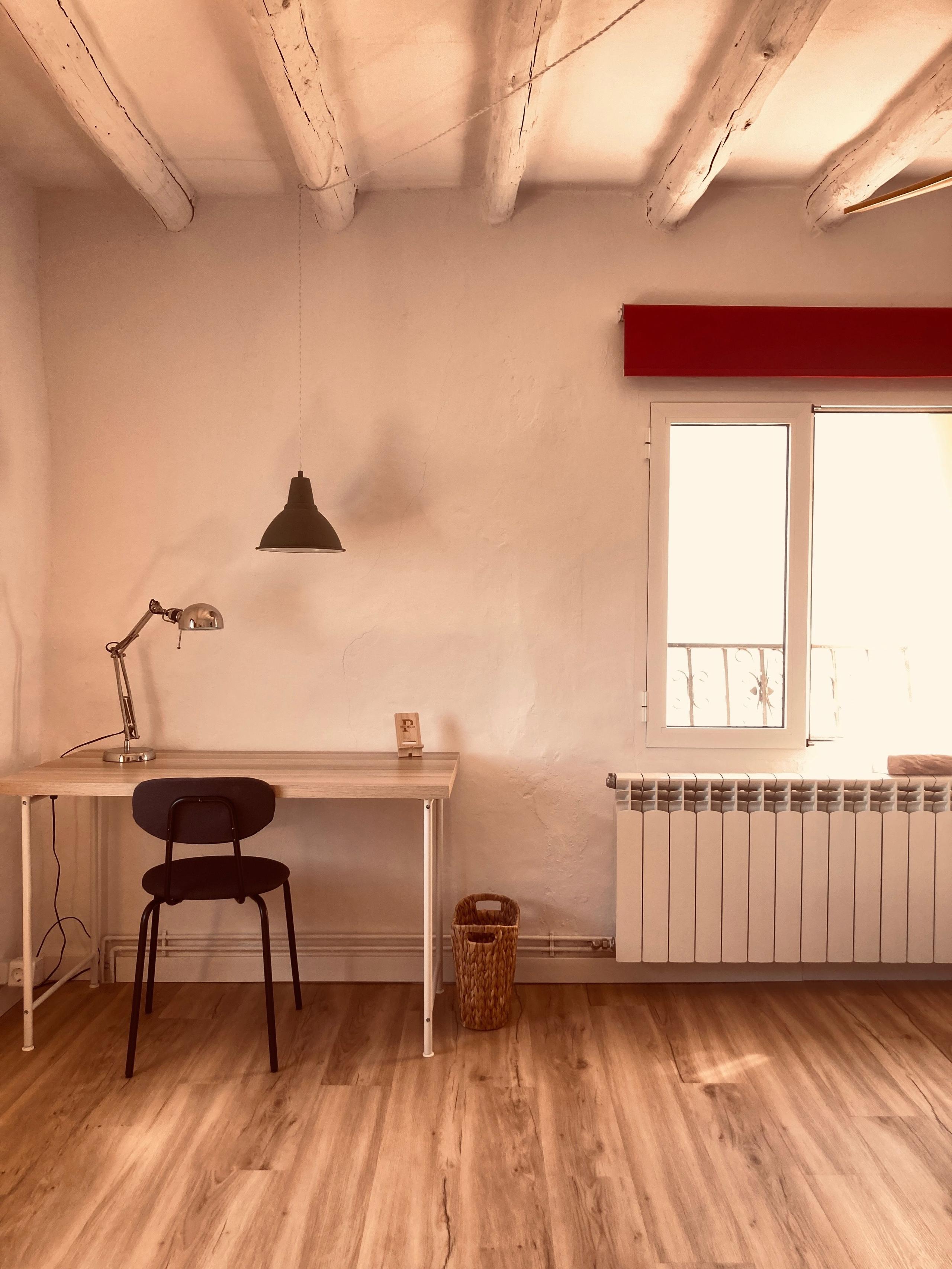 Work desk with lamp and chair, street-facing window with blind and wooden beams in La Rinko room