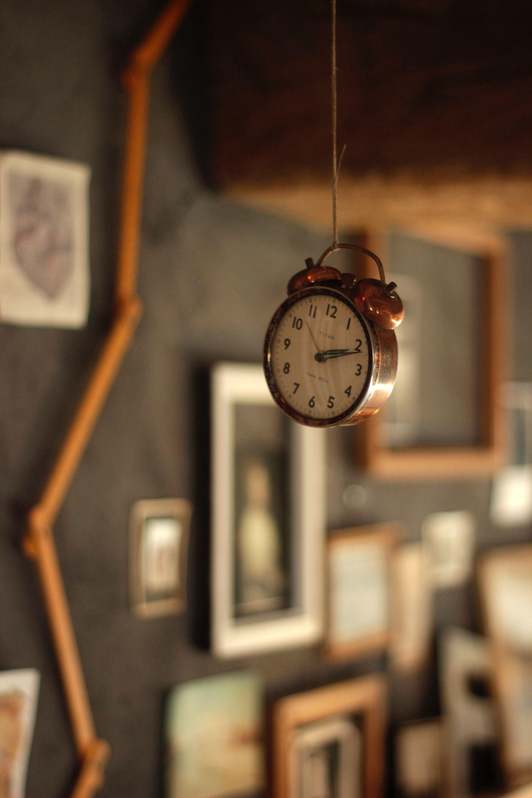 A wind-up clock suspended from the ceiling by a thread, with photos of El Granero in the background