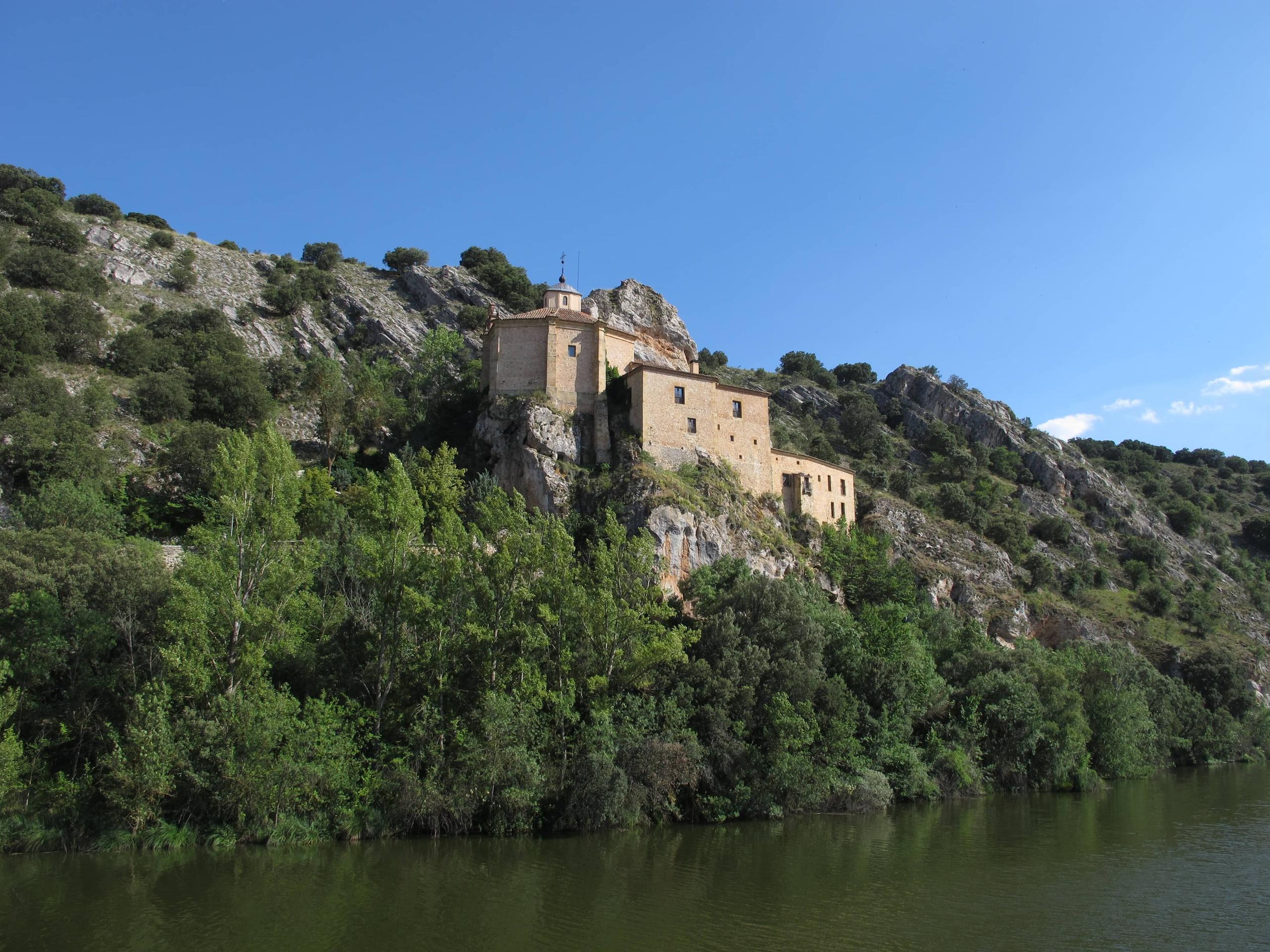 Ancient building on a mountaintop surrounded by vegetation and clear water — Ermita de San Saturio in Soria