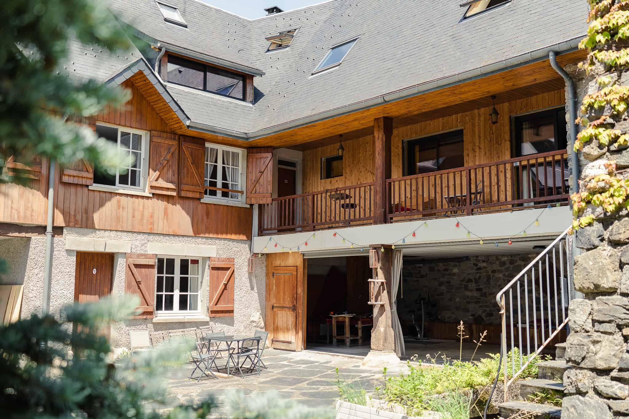 Exterior view of the Pyren'Escape mountain chalet showing the courtyard with wooden balcony, stone walls, and outdoor seating area